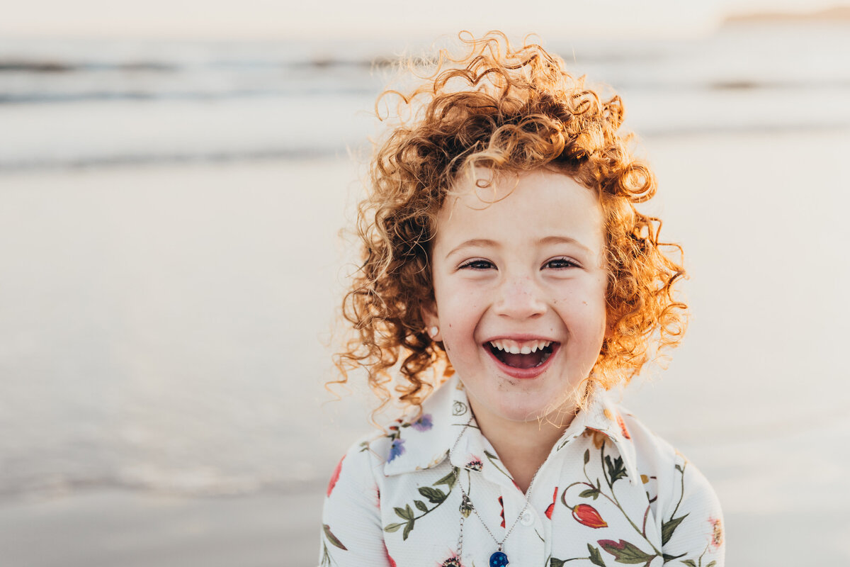 A vivacious red-headed girl smiles on the beach in San Diego.
