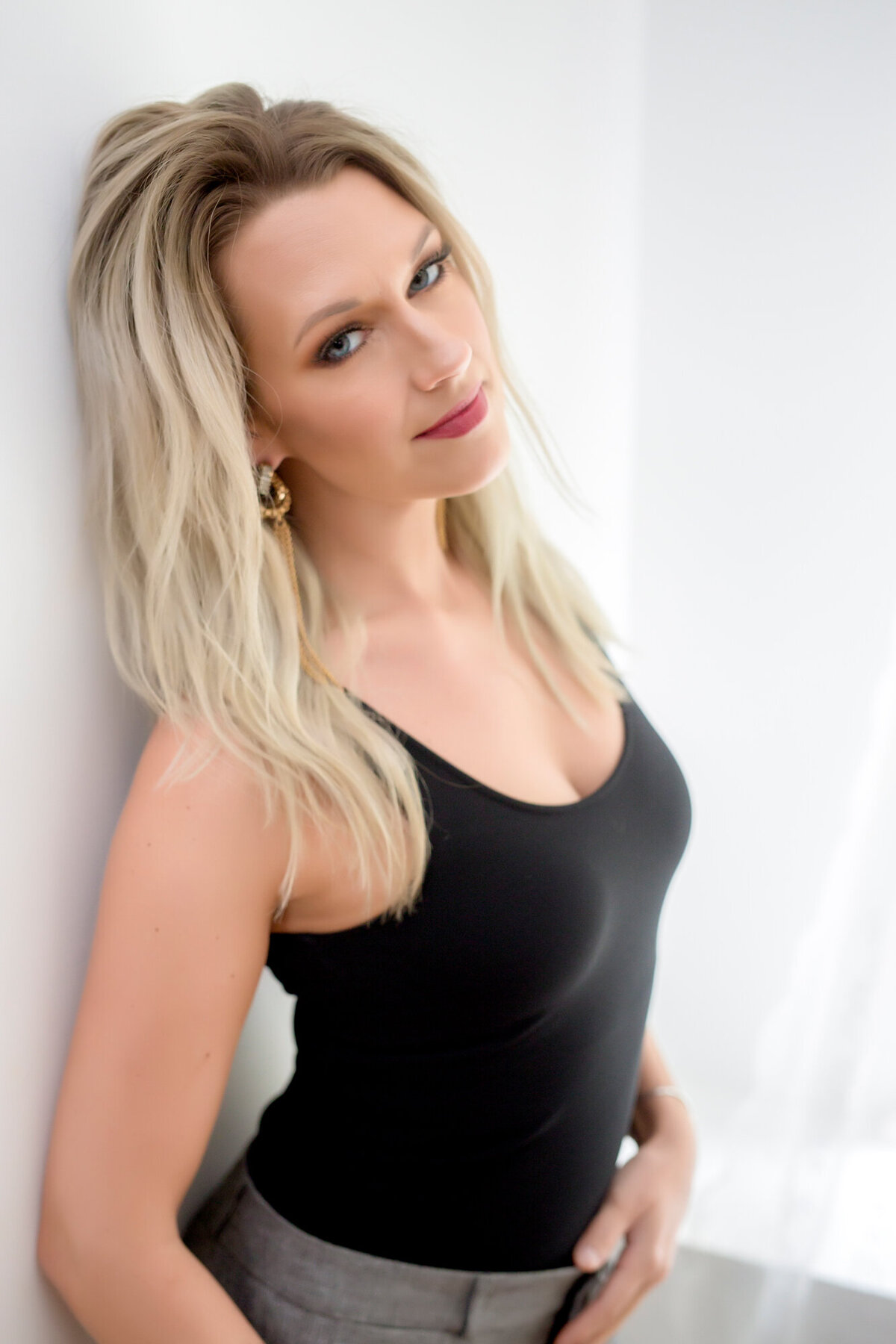 Female headshot client leaning against a wall wearing a black tank top