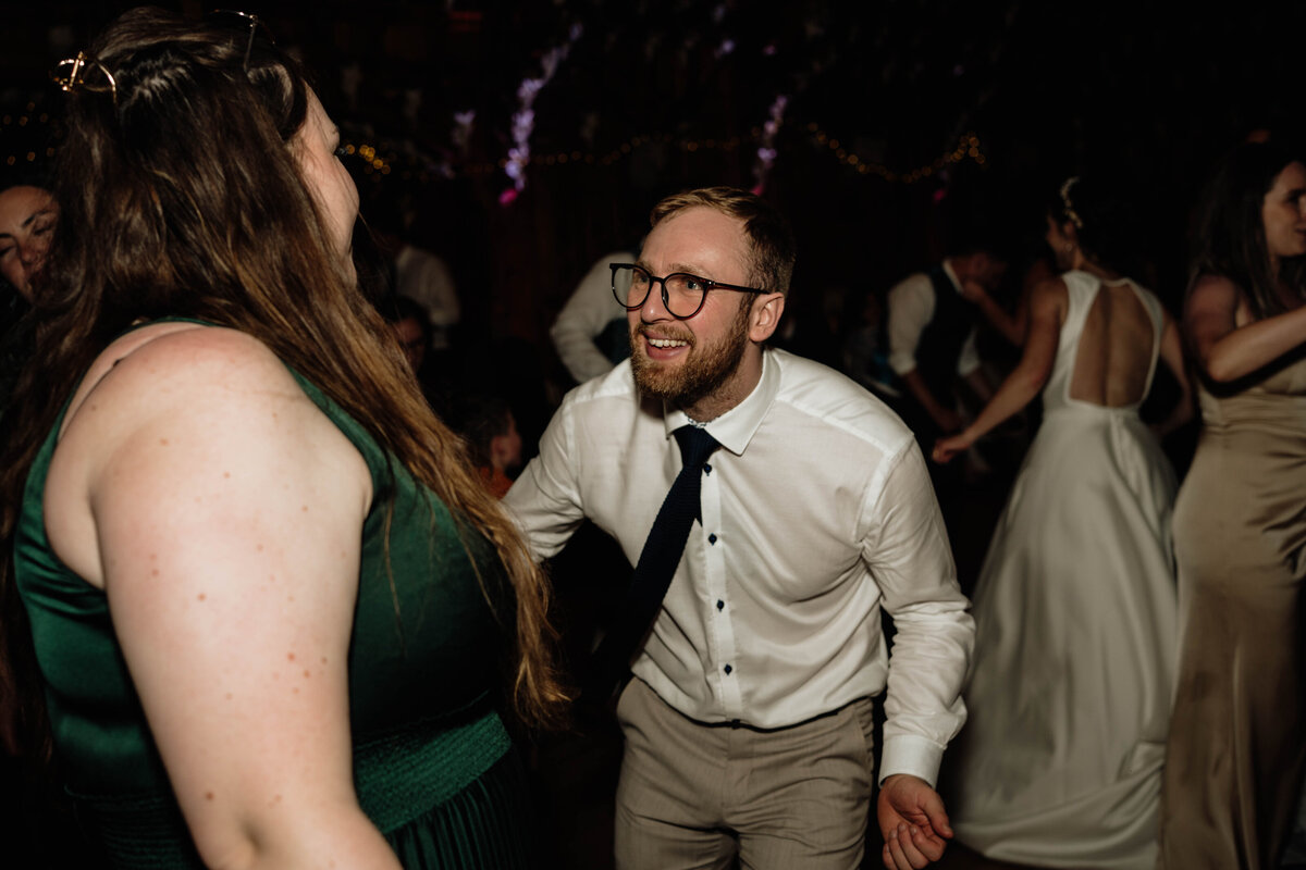 A wedding guests is photographed dancing to music at an evening wedding reception.