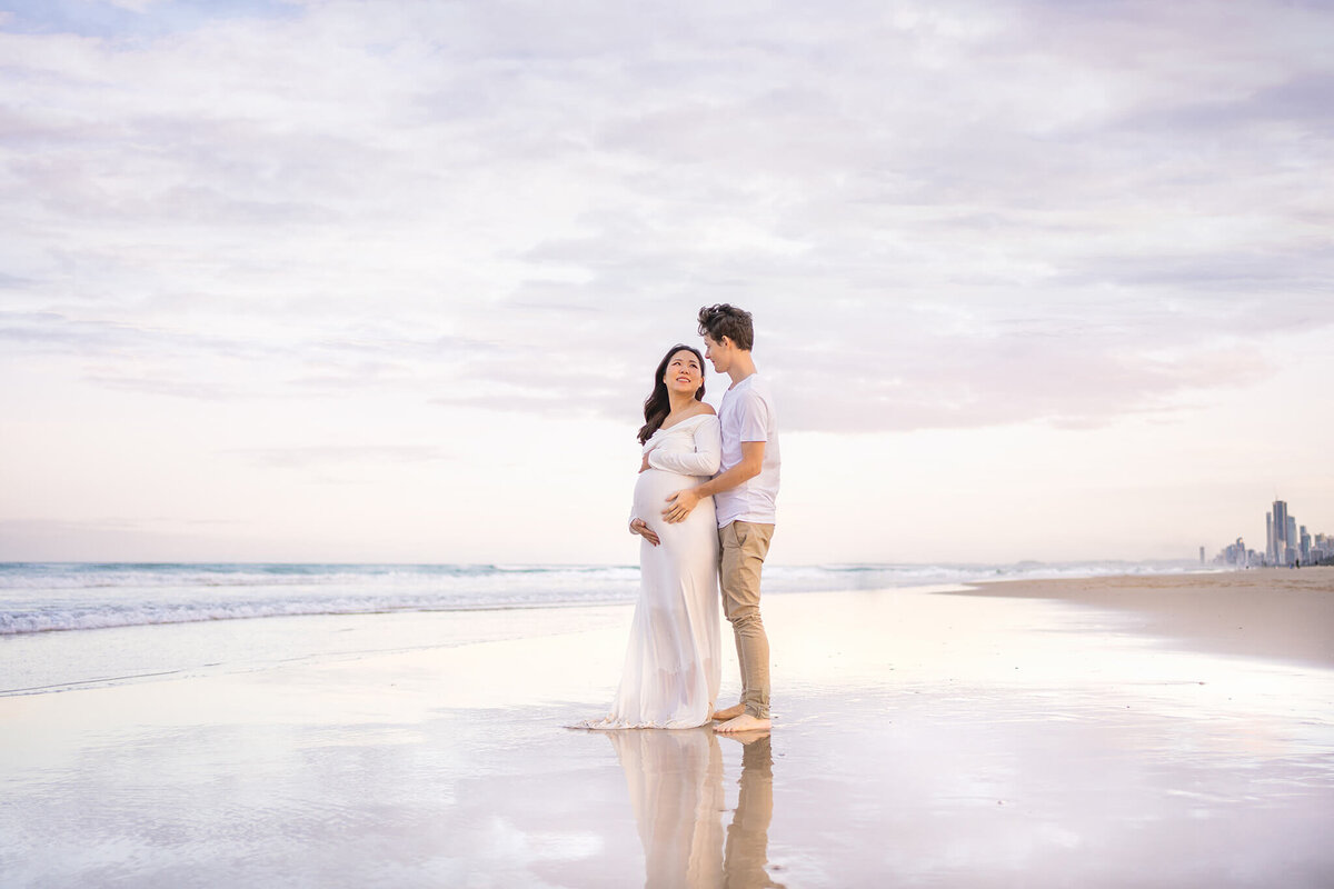Couple sharing intimate moment on the beach at The Spit during maternity photoshoot