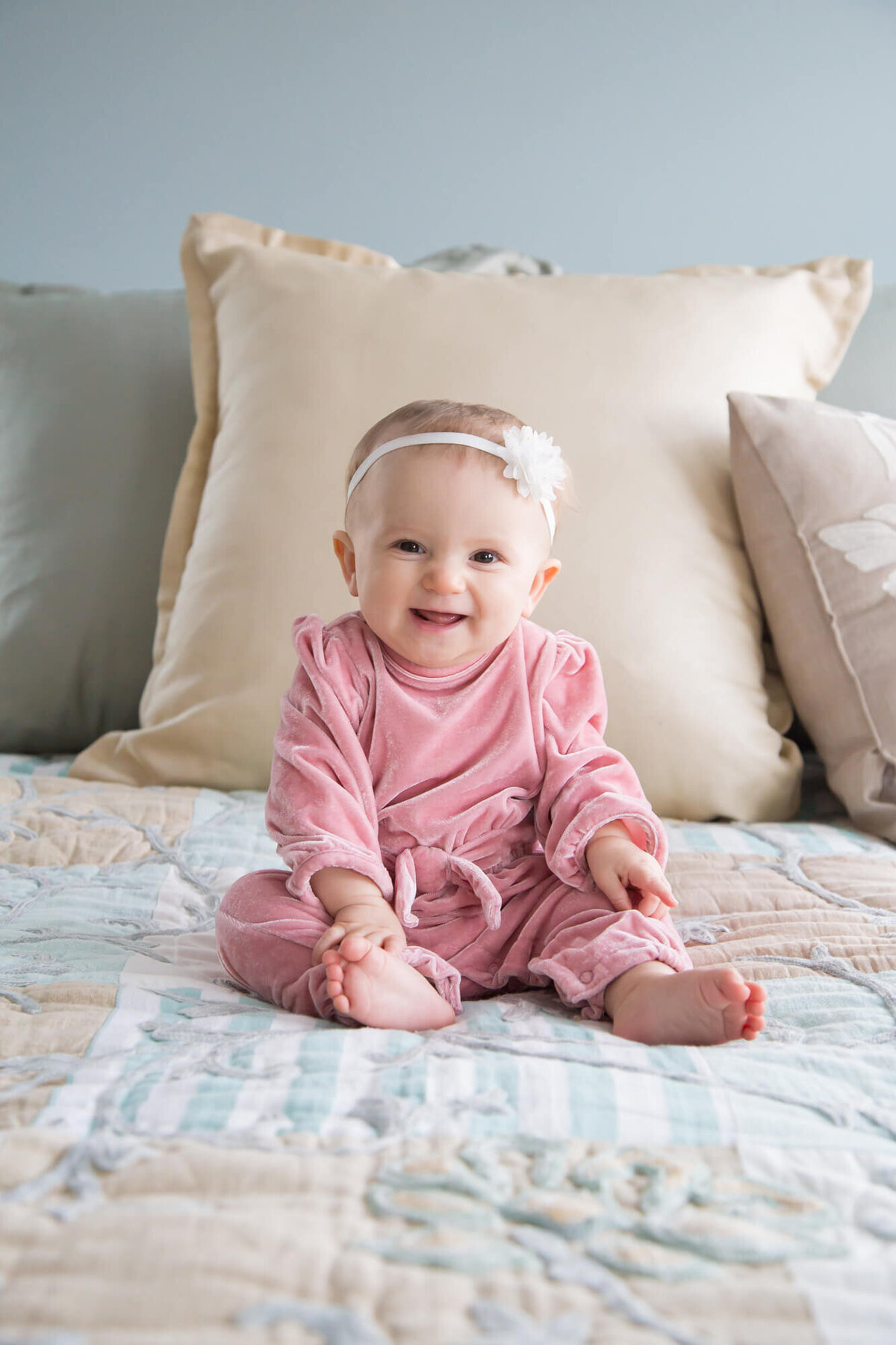 joyful one year old baby sitting up in a pink romper on bed