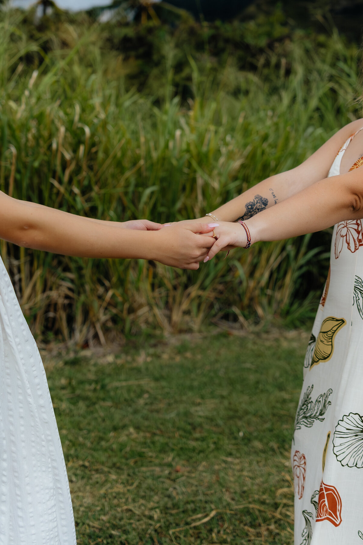 Close-up of two best friends holding hands in a grassy field at Kualoa Regional Park during a true-to-color photoshoot on Oahu, Hawaii.