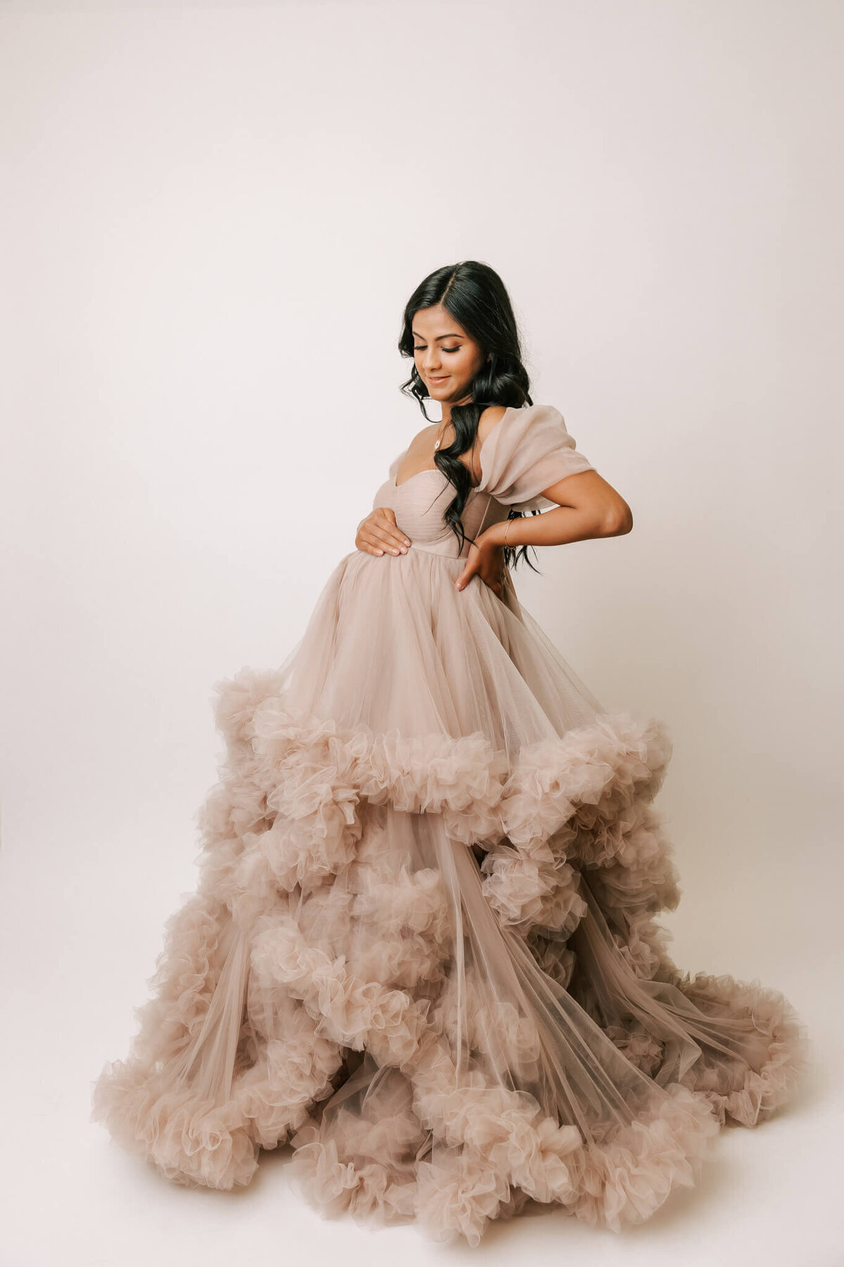 woman with long black hair smiling looking down at belly in tan gown in portland maternity session by photographer Ann Marshall's studio.