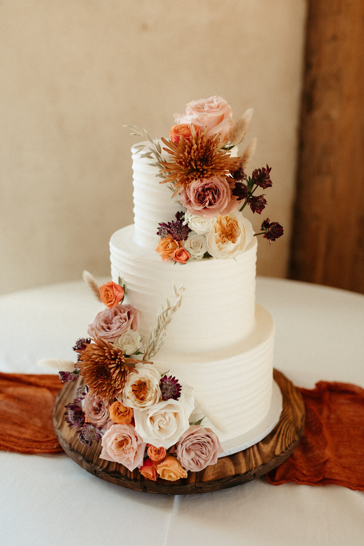 Simple three tier wedding cake with golden and rust colored flowers for decorations