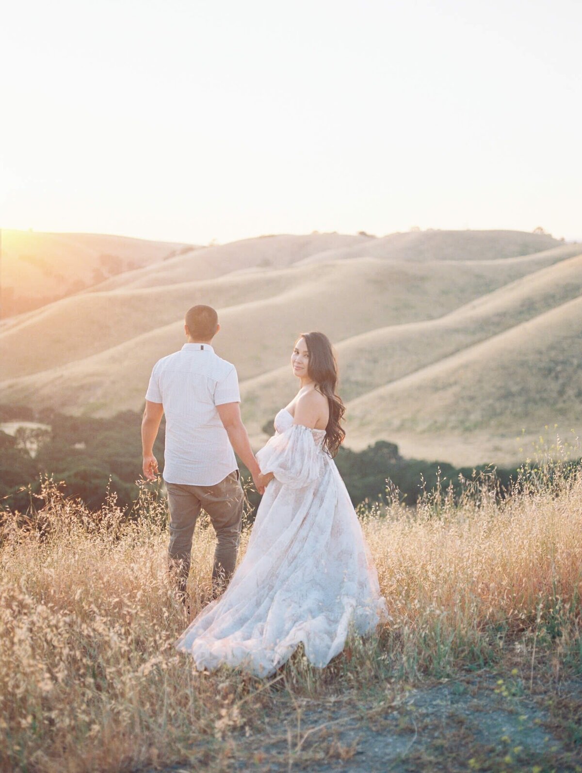 Maternity photoshoot in San Francisco with a pregnant woman and expecting dad standing in a field against hills.