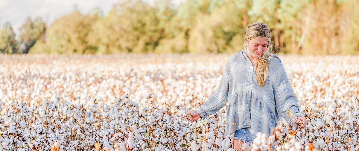 teenage girl walking thru cotton field closely examining the cotton