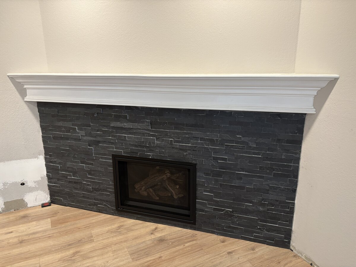 A remodeled fireplace featuring dark stacked stone tile, a white mantel, and updated flooring in an East Bay home.