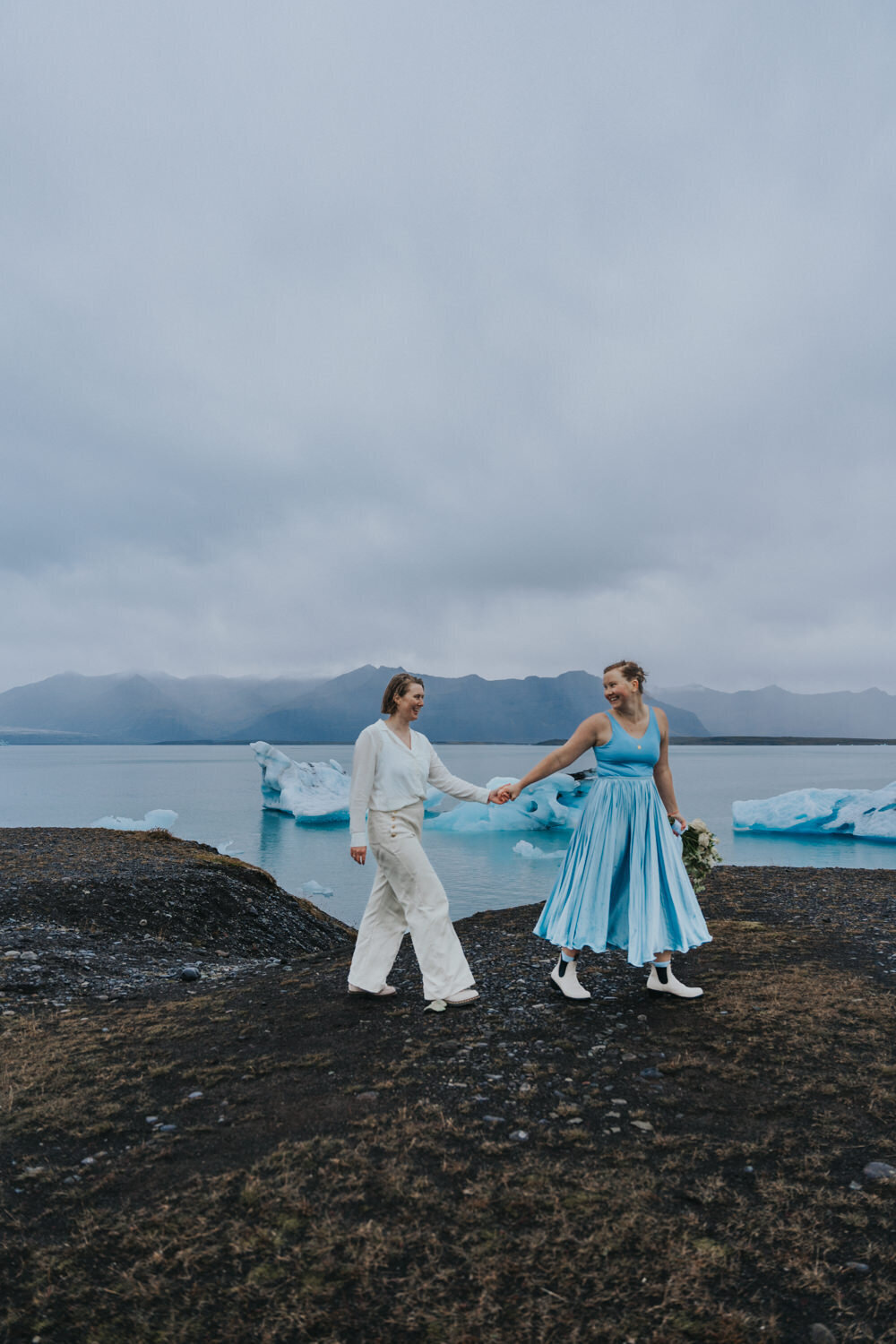 Women walk down the Black Sand Beach of Iceland hand in hand 