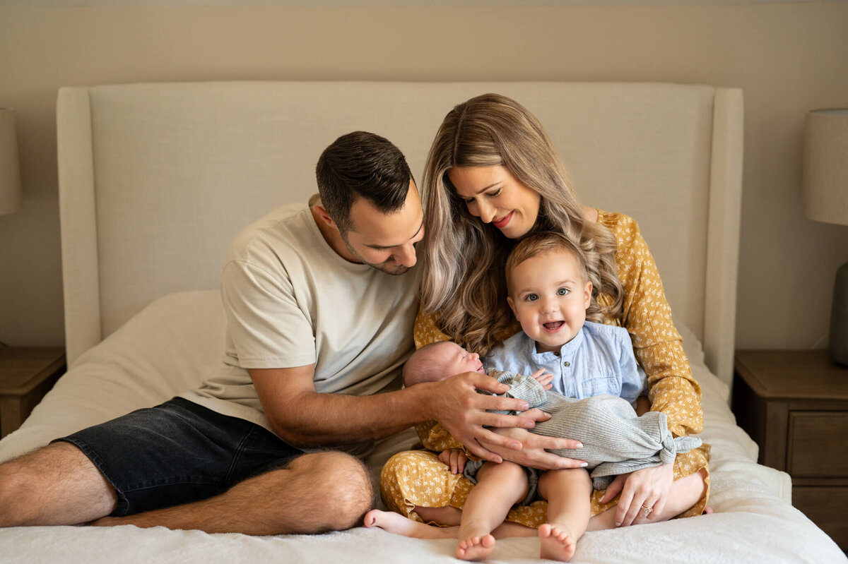family snugging with newborn on the bed