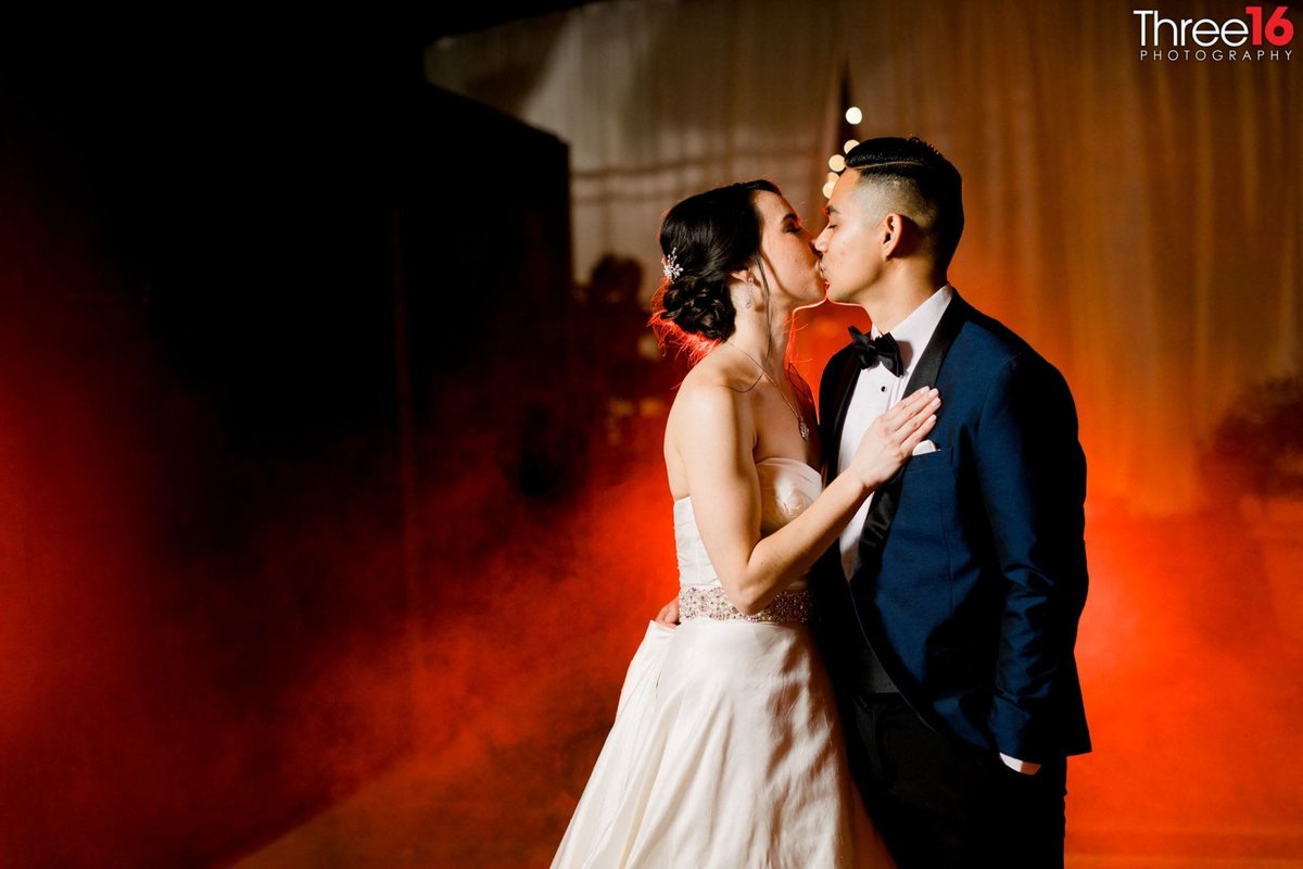 Newly married couple share a kiss with red smoky fog in the background