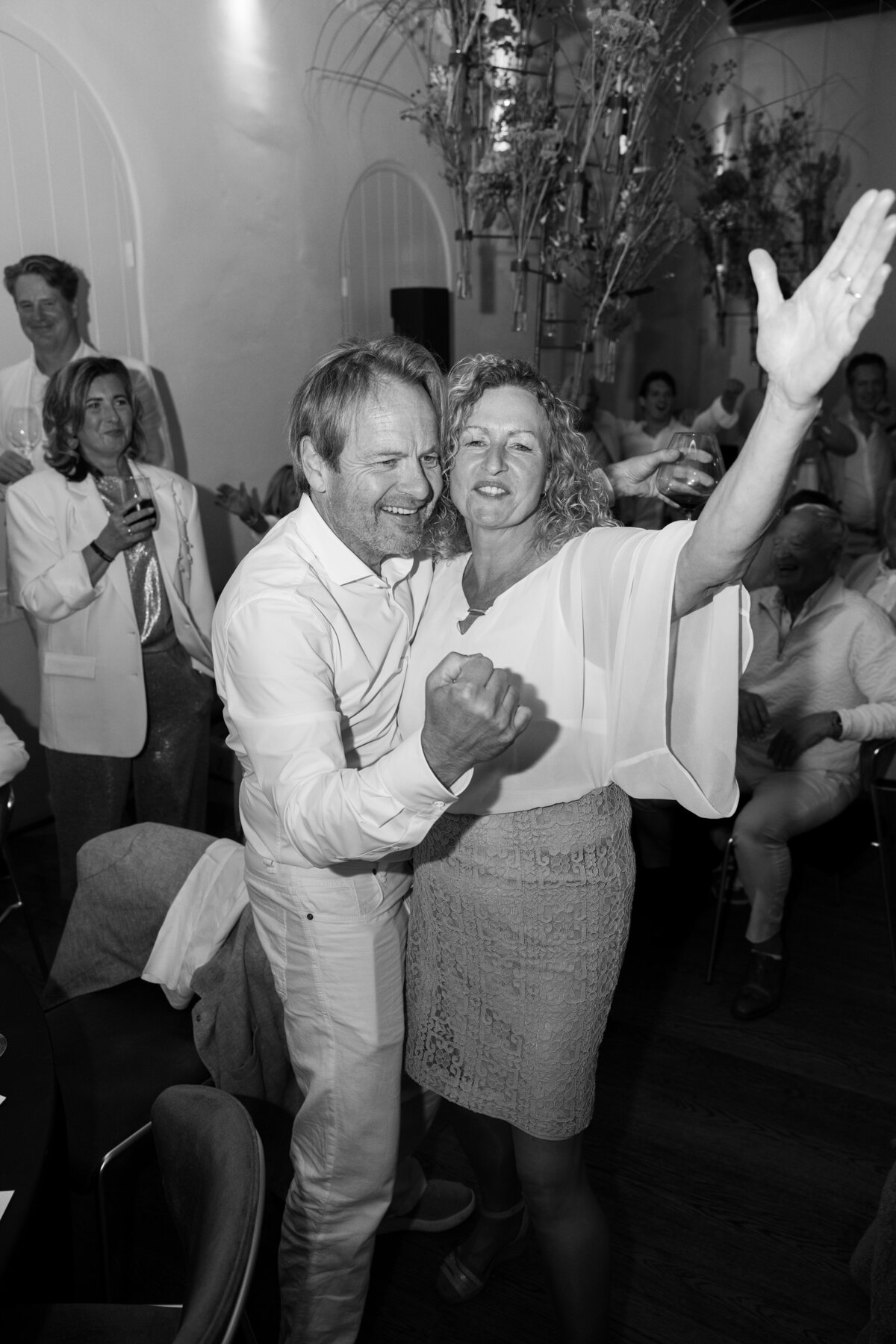 A joyful moment on the dance floor, featuring a couple immersed in the celebration. Their expressions of happiness and the energy of the crowd are perfectly captured in this black-and-white photo, reflecting the lively atmosphere of the event.