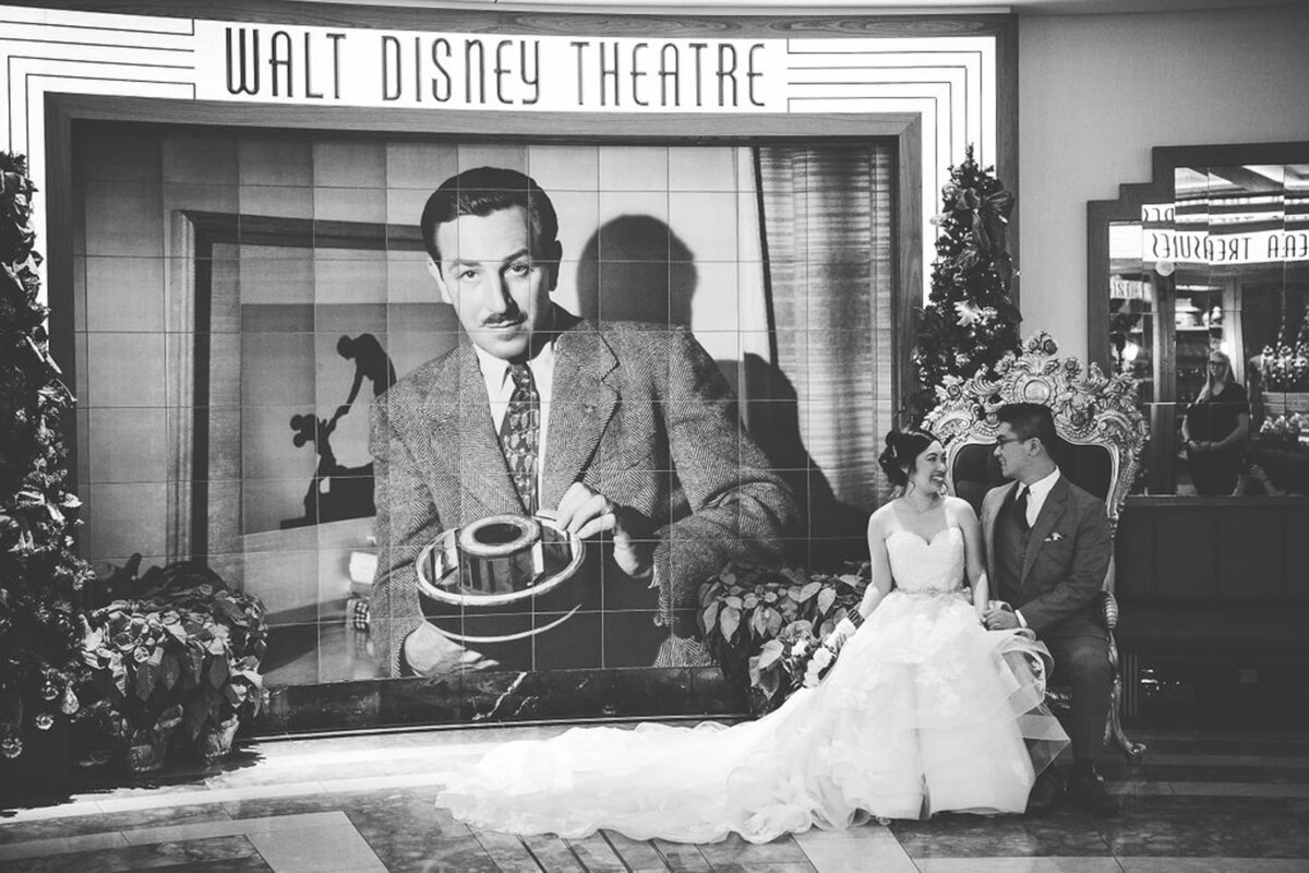 Black and white of bride and groom sitting beside photo of Walt at Walt Disney Theater on Disney Dream