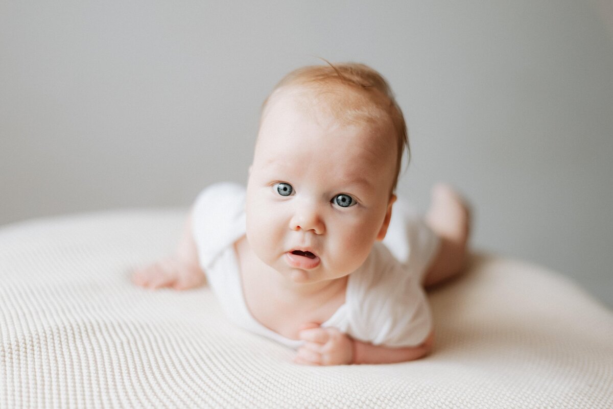 Baby girl laying down on the blanket looking up at milestone photoshoot in Billingshurst