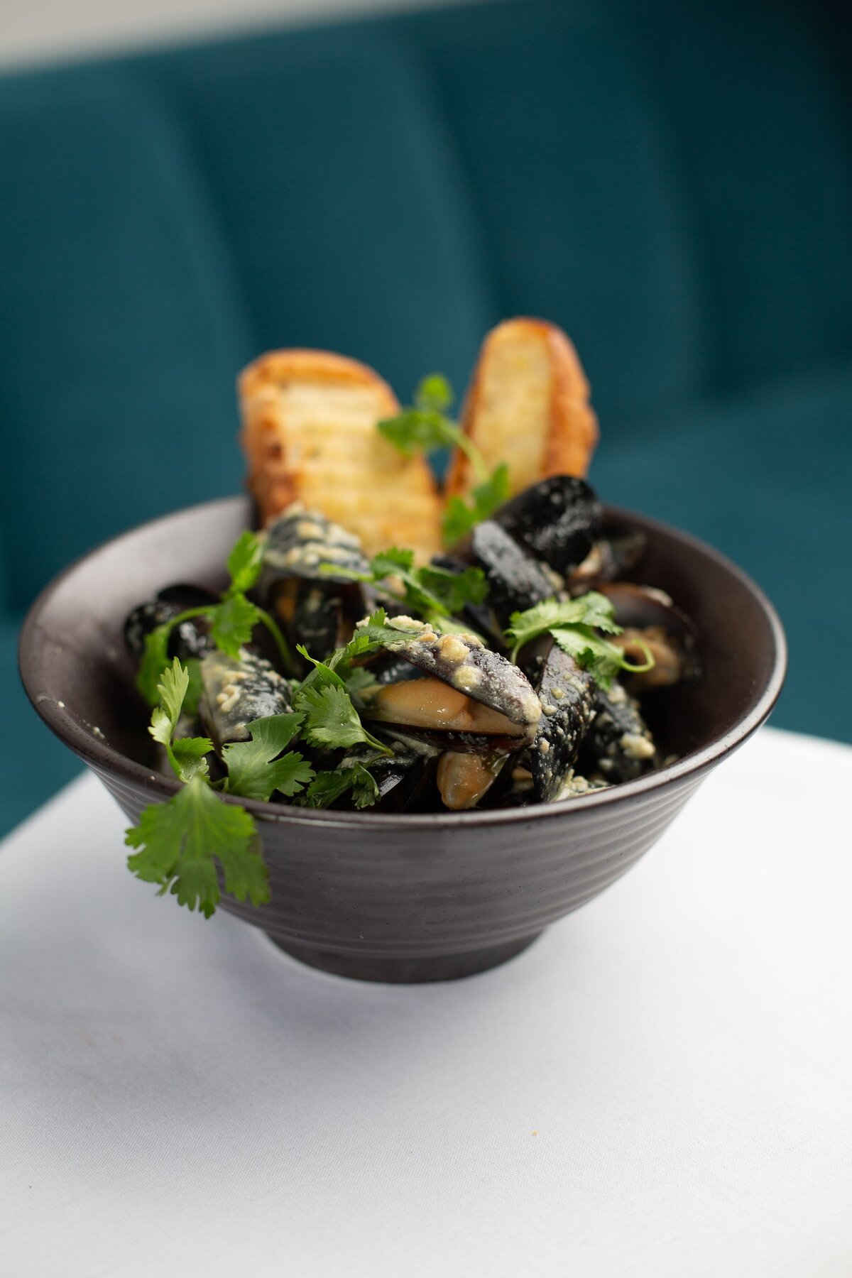 dark ceramic bowl full of mussels with bread against teal velvet