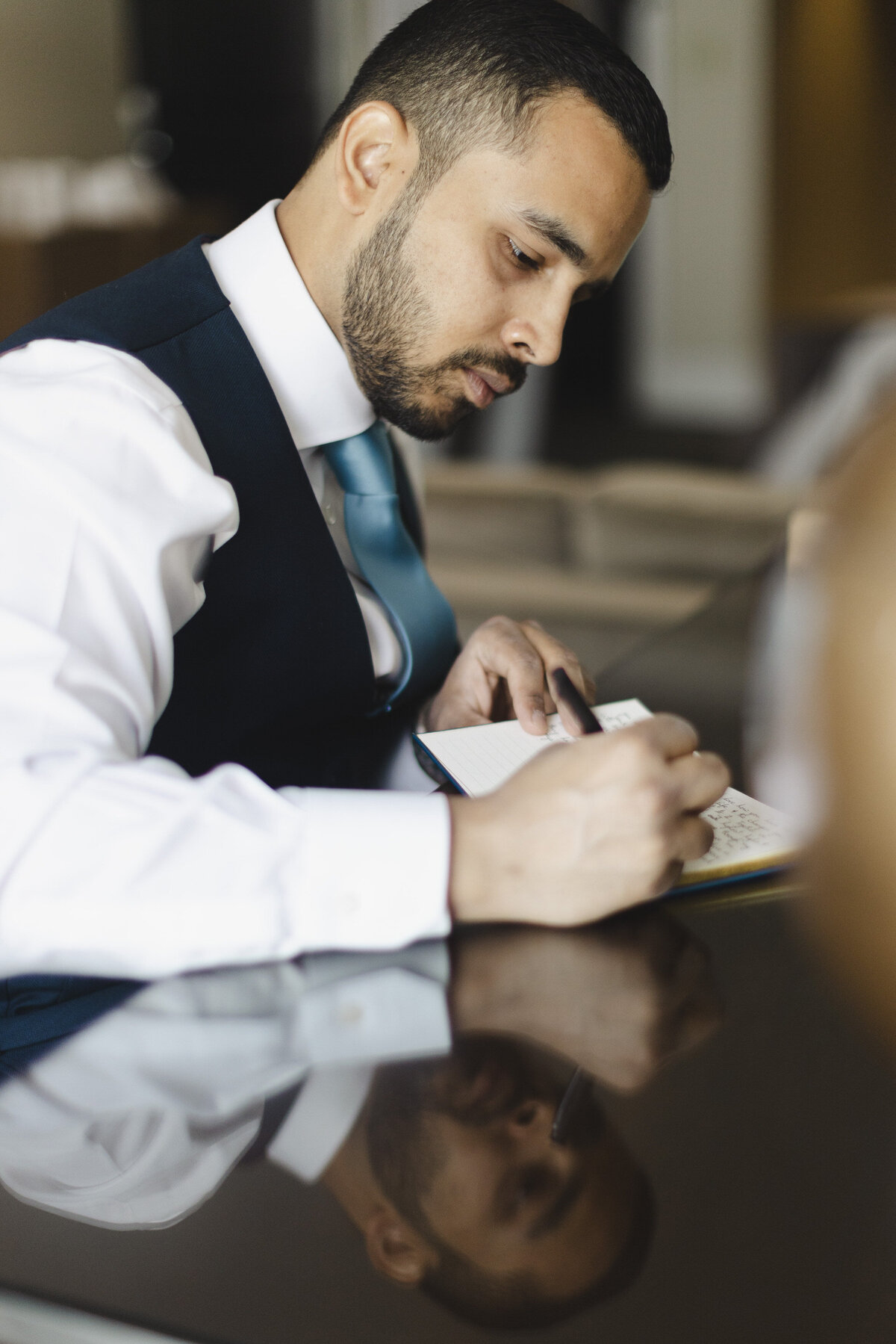 A person in a suit sitting down and writing in a small notebook 