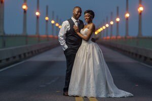Professional St Augustine wedding photography showing newlywed couple embracing on historic bridge at sunset with string lights