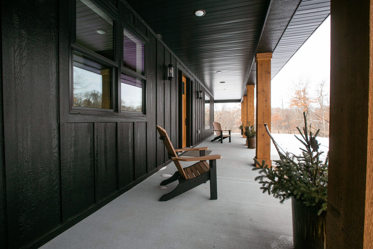 Exterior view of custom home in Elk River, Minnesota with black siding, wood details and front porch built by Cornerstone Custom Builds