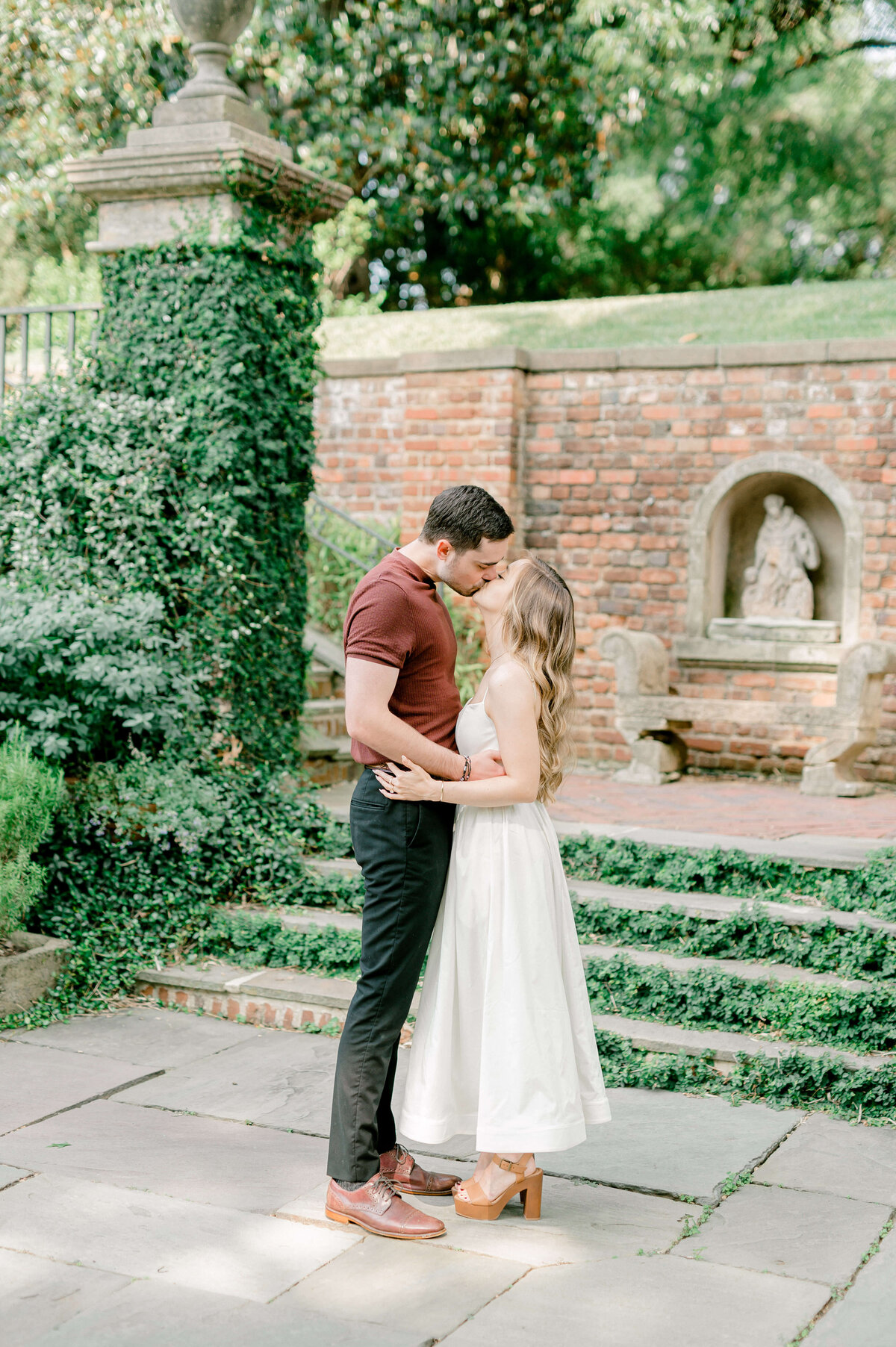 Portrait of a couple kissing in a garden with brick and ivy in the background.