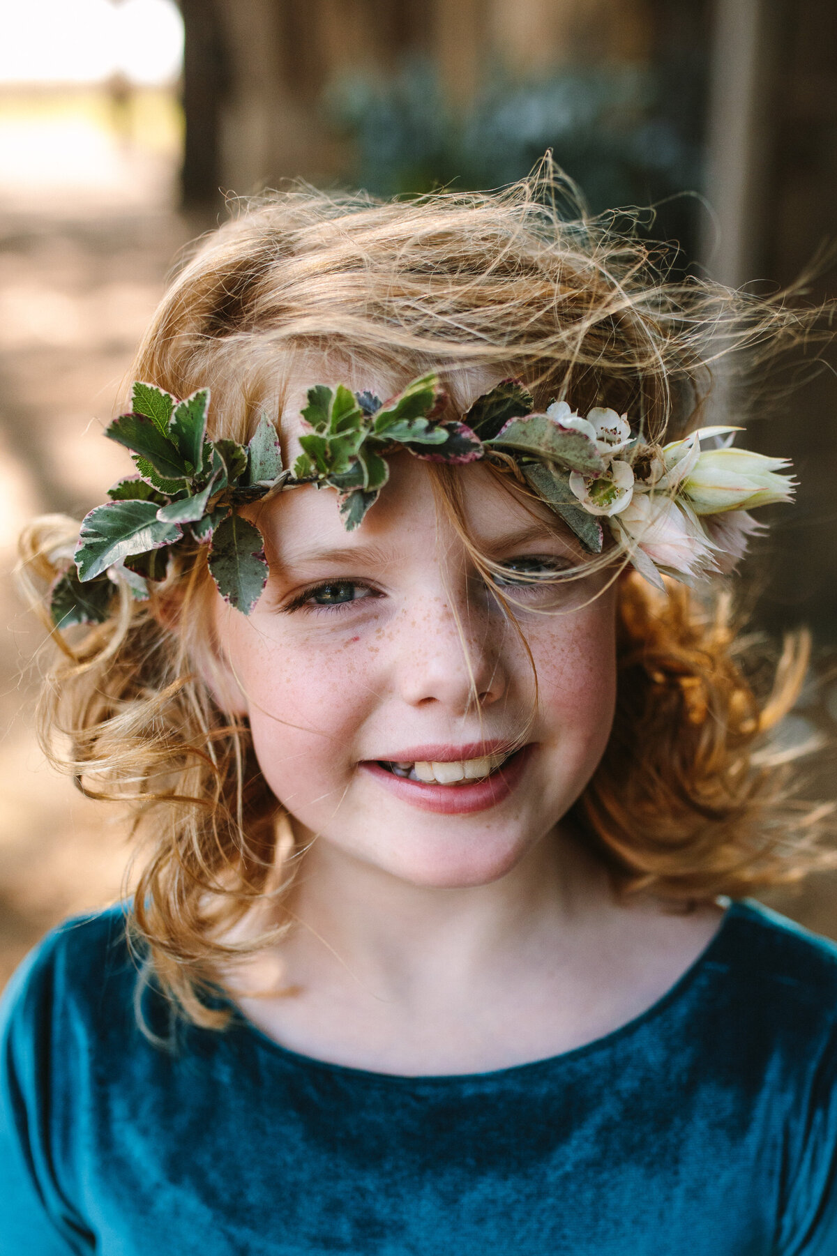 A young flower girl smiles with her hair blowing in the wind. 