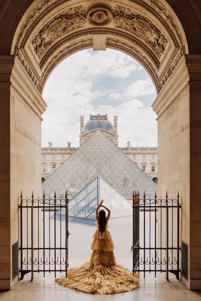 Luxury portrait session at the Louvre Paris featuring woman in golden princess gown facing iconic pyramids