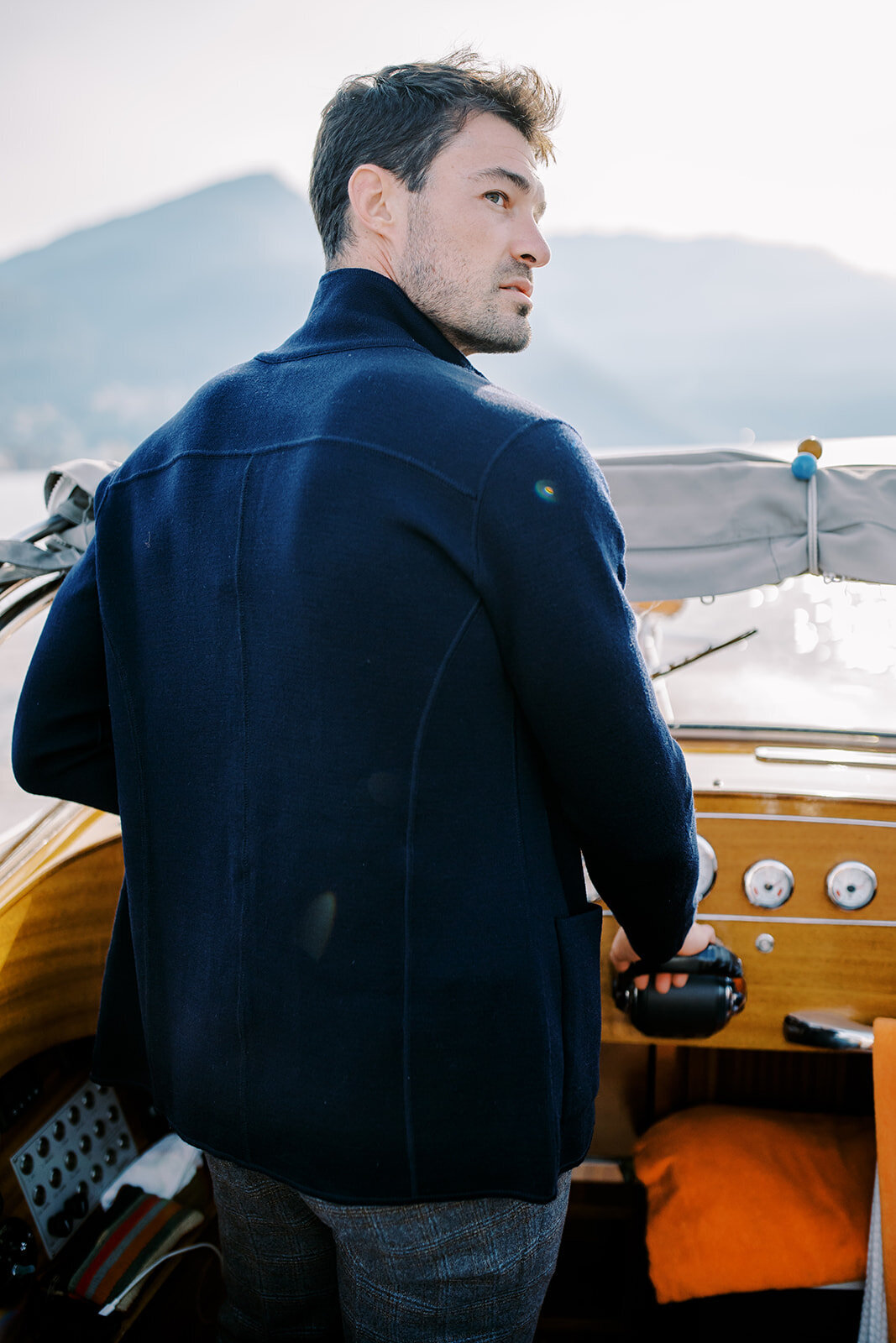 Film photograph of bride and groom on a wooden boat on Lake Como in Italy she is wearing a white halter jumpsuit with her hair down in loose waves and he is wearing grey and navy cashmere sweater and coat photographed by Italy wedding photographer