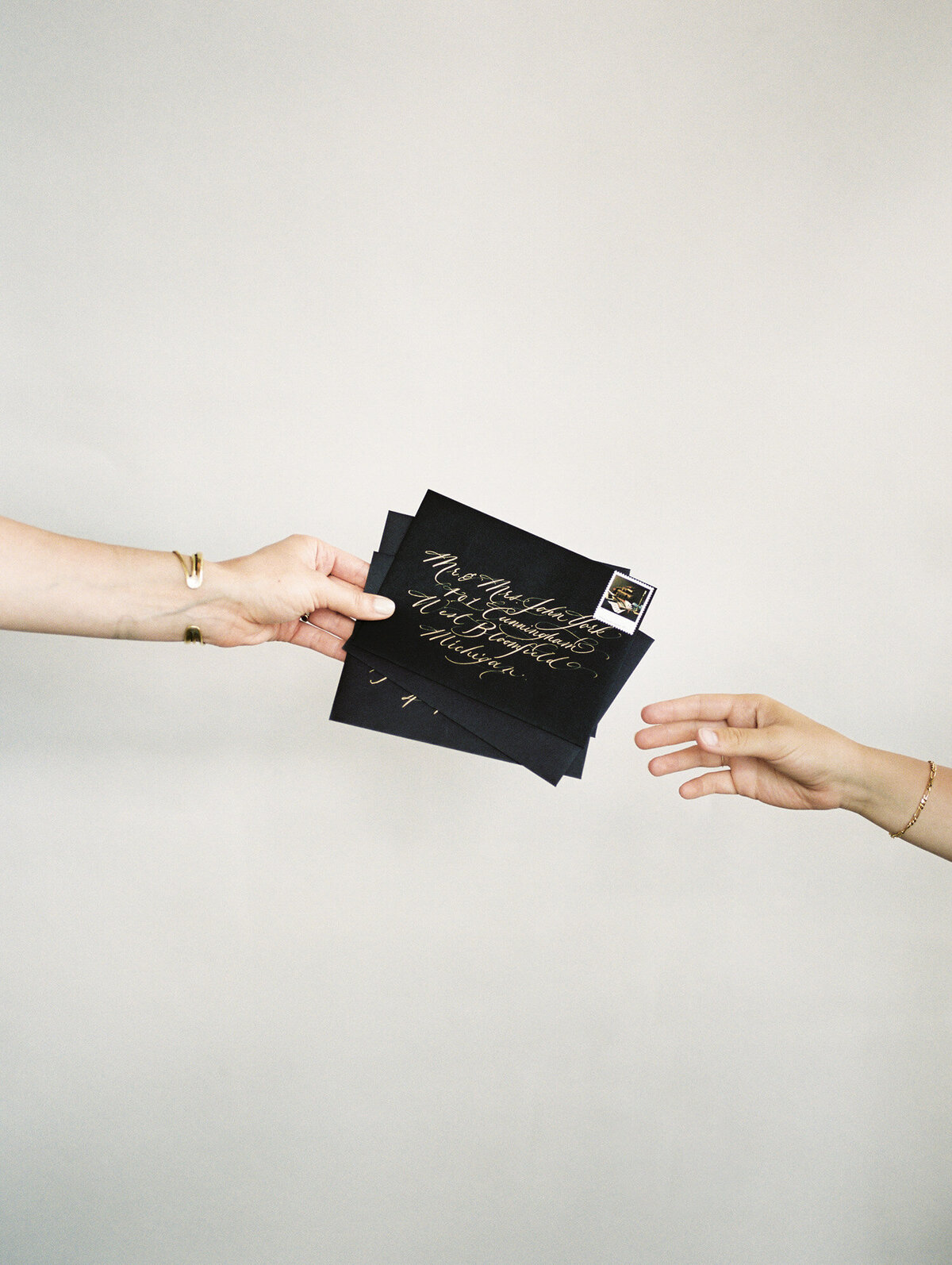 woman's hand holds black stationery envelopes with gold ink calligraphy to another woman's open hand, film calligrapher brand photo