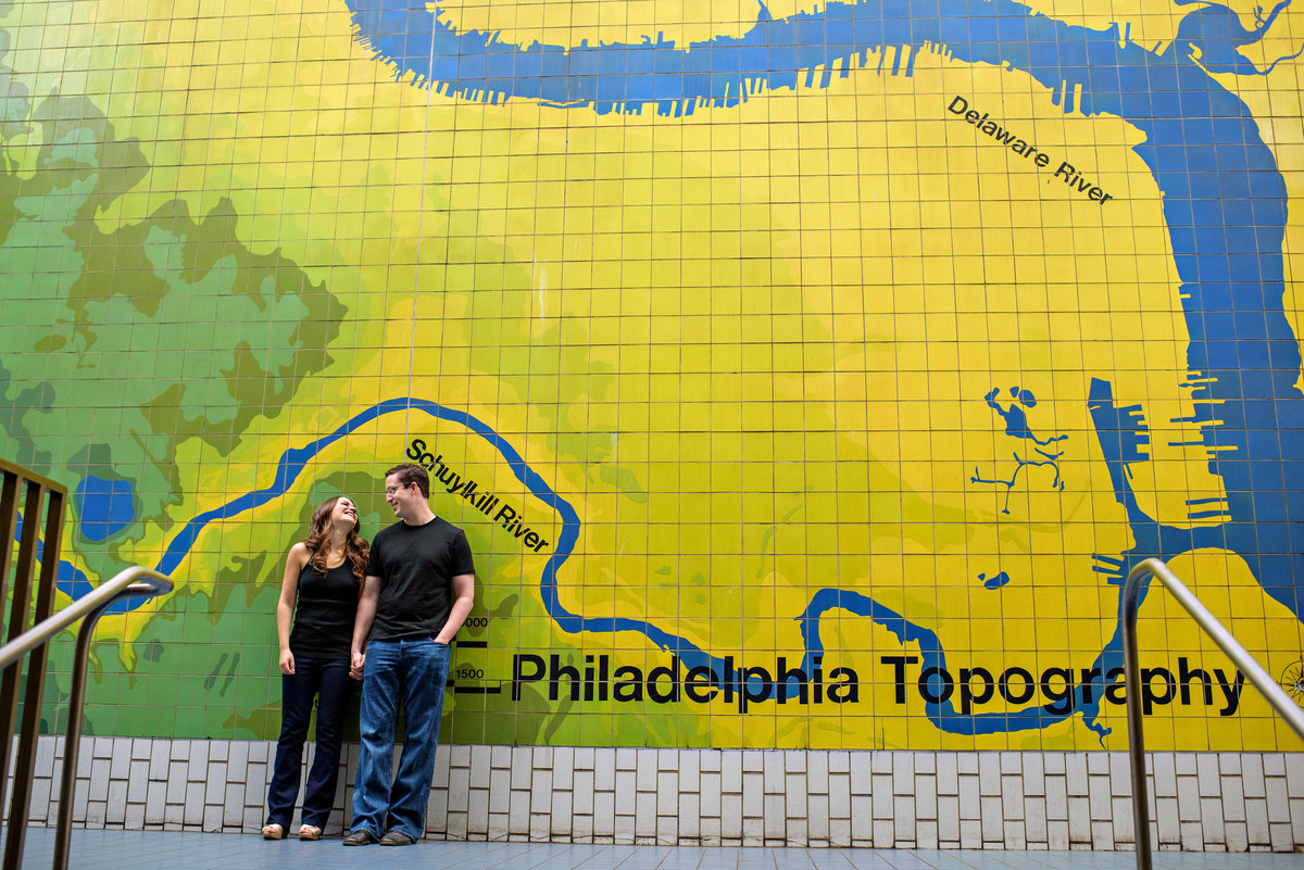 A man and woman lean against a philly mural in the subway.