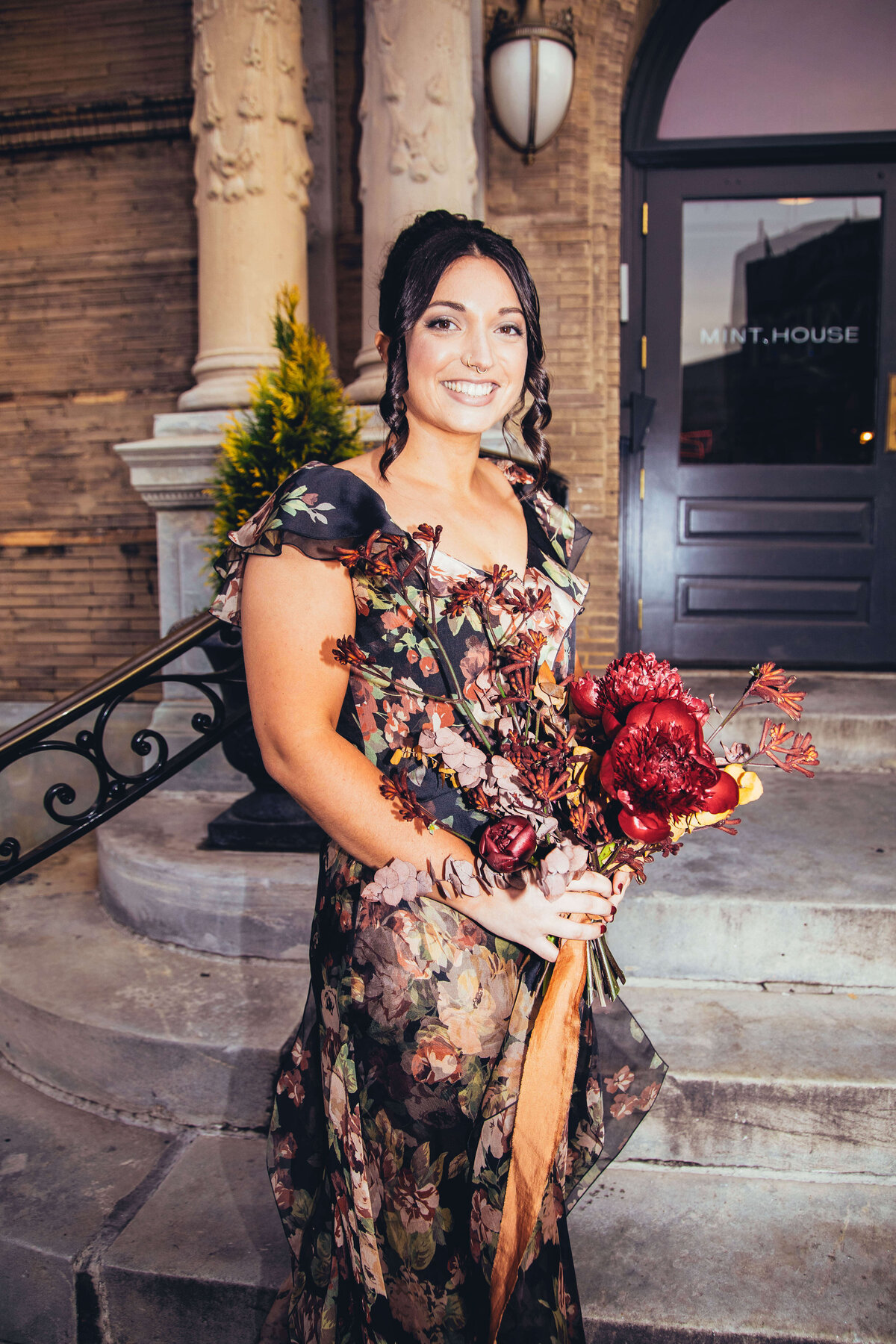 Bride wearing a floral dress and holding a tried flower bouquet by Jessamine