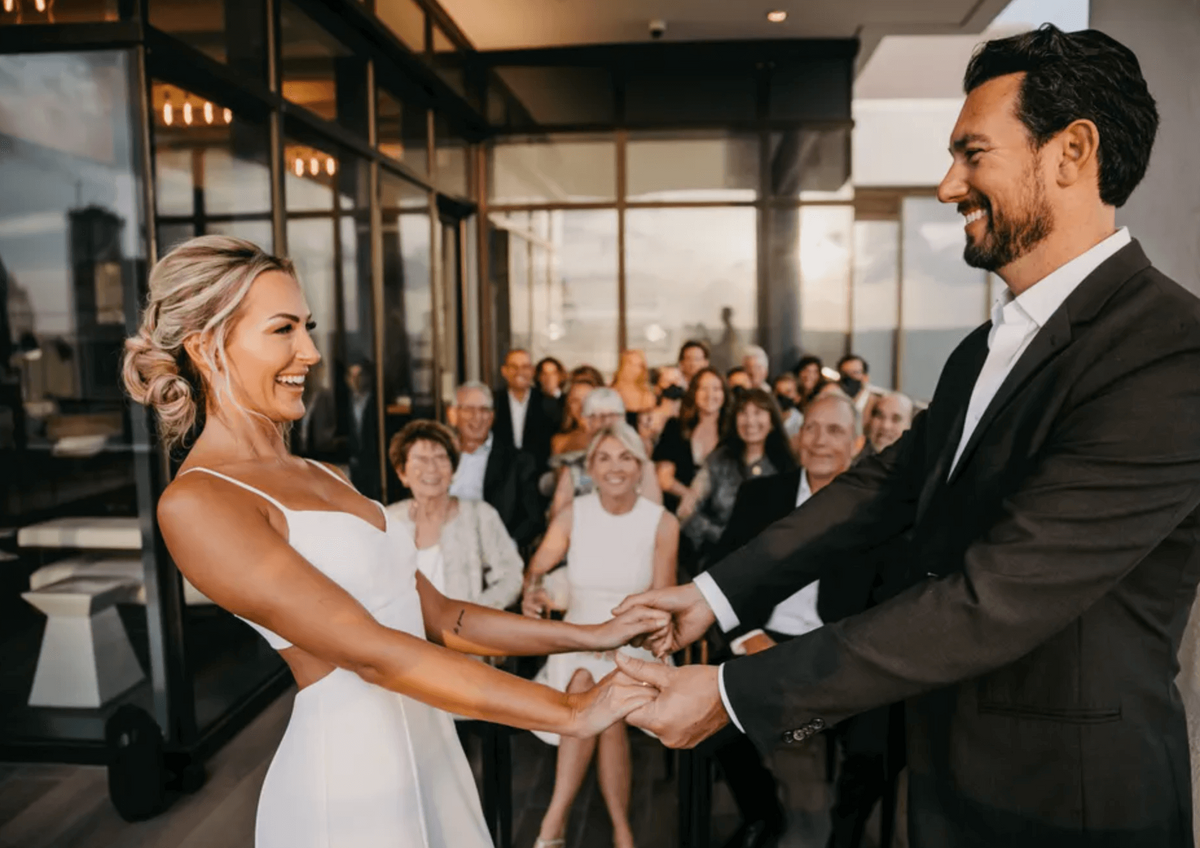 Bride with elegant updo and groom with fresh men’s haircut exchange vows at sunset wedding in Austin with guests smiling behind them