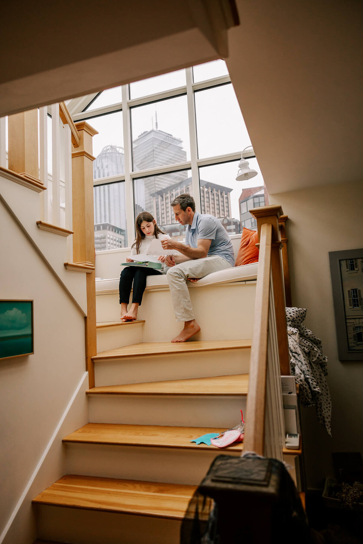 Dad helps his daughter with her homework. They are sitting in the bay window of their South End home, the Boston skyline behind them.