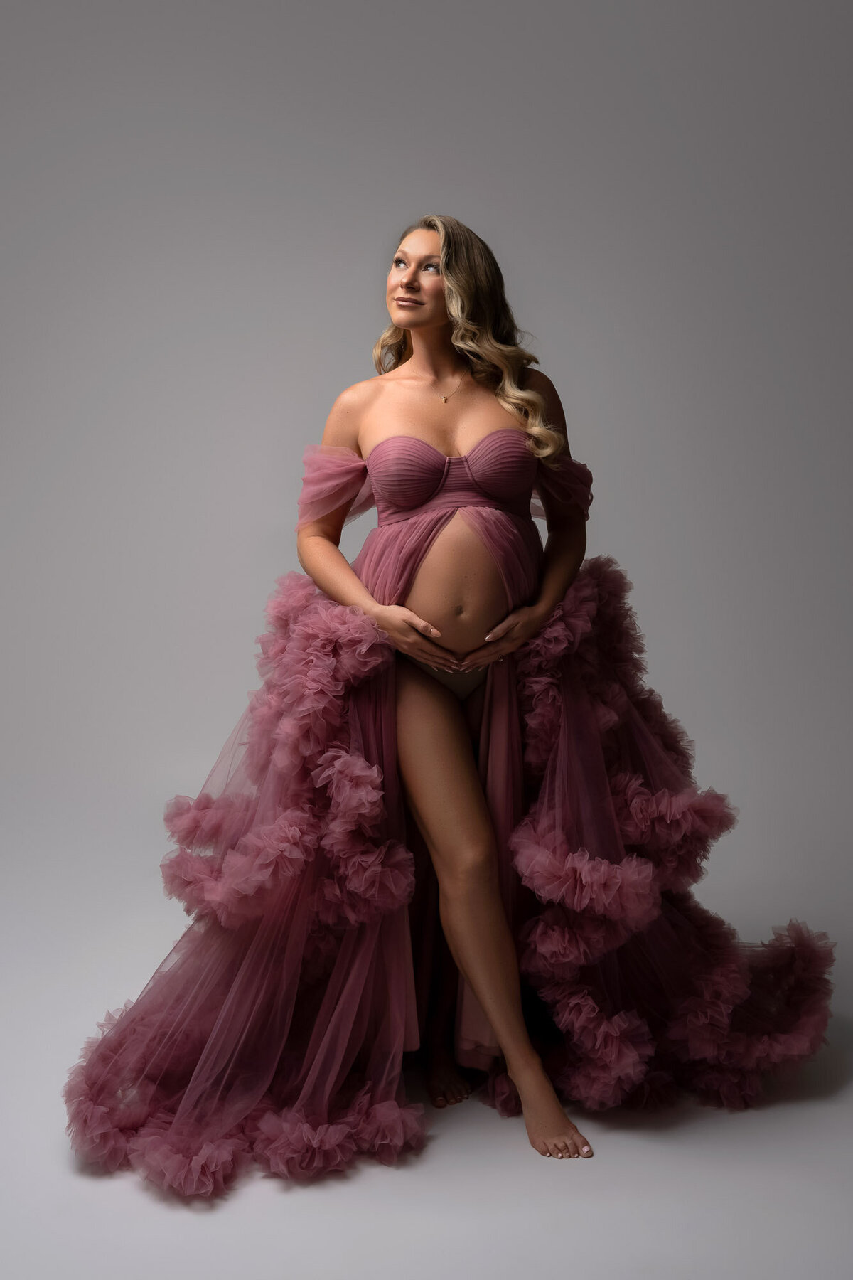 Elegant maternity portrait featuring pregnant woman in purple gown with dramatic studio lighting