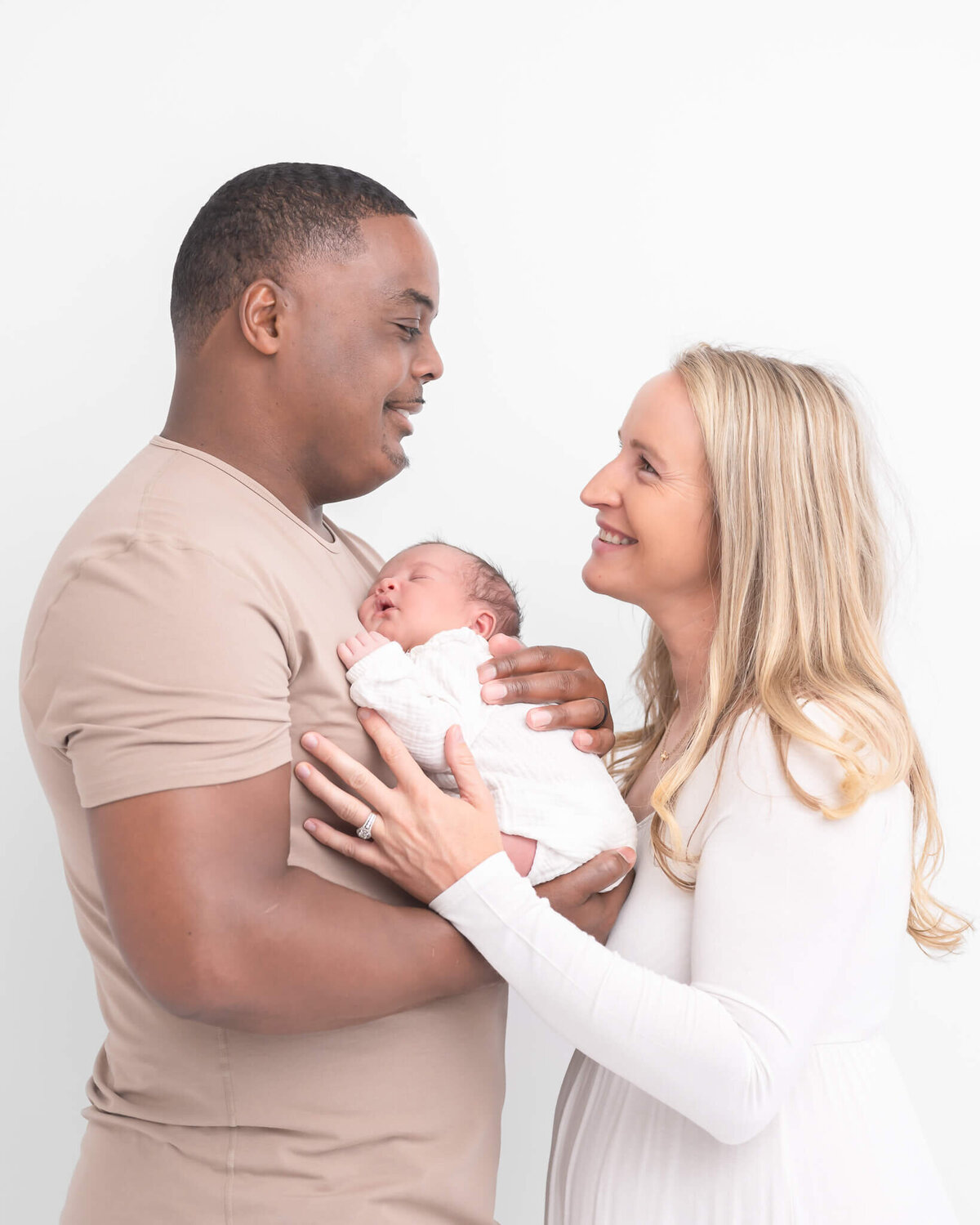 Mom and dad holding new baby in gorgeous light bright studio session with timeless elegant feel