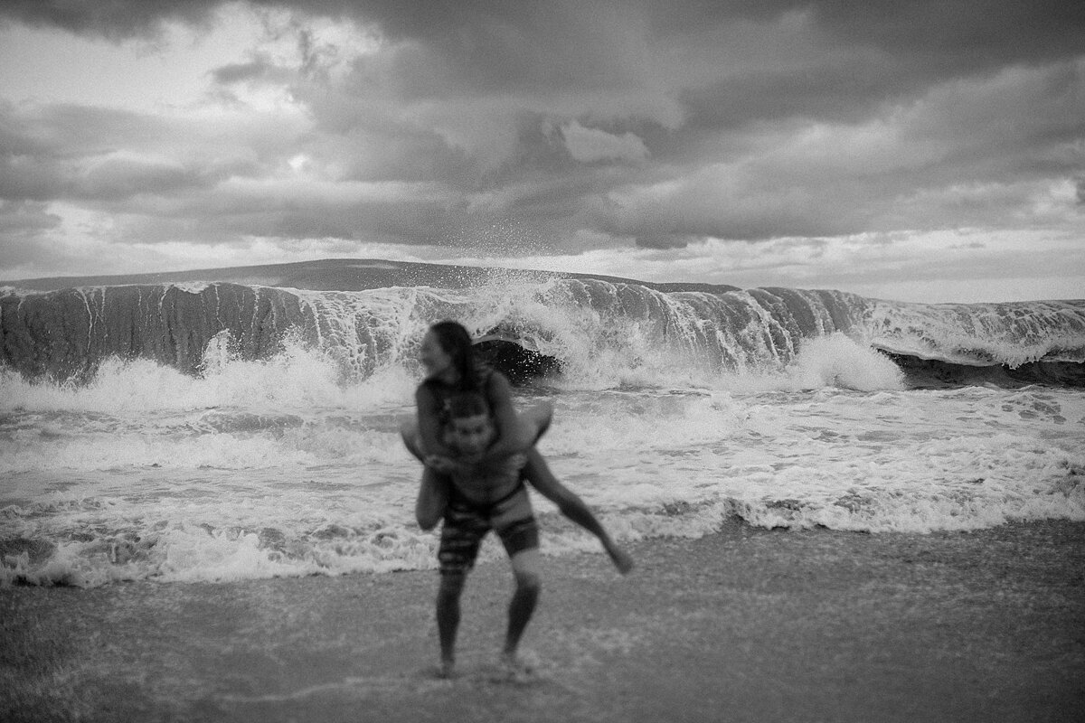 Large waves crash behind a couple goofing around on the beach in Makena on the island of Maui