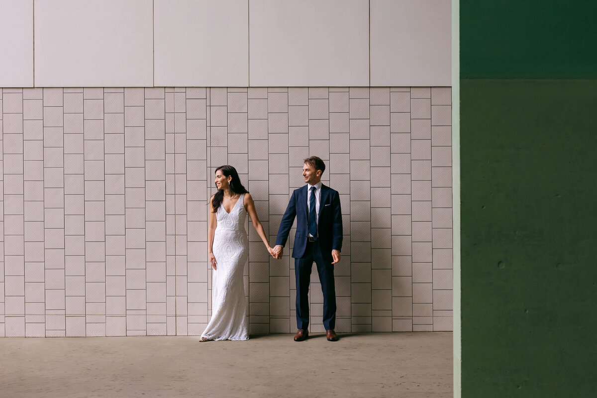 Bride and groom holding hands in front of a modern tiled wall at GOMA South Bank — Brisbane wedding photography by Leanne J.