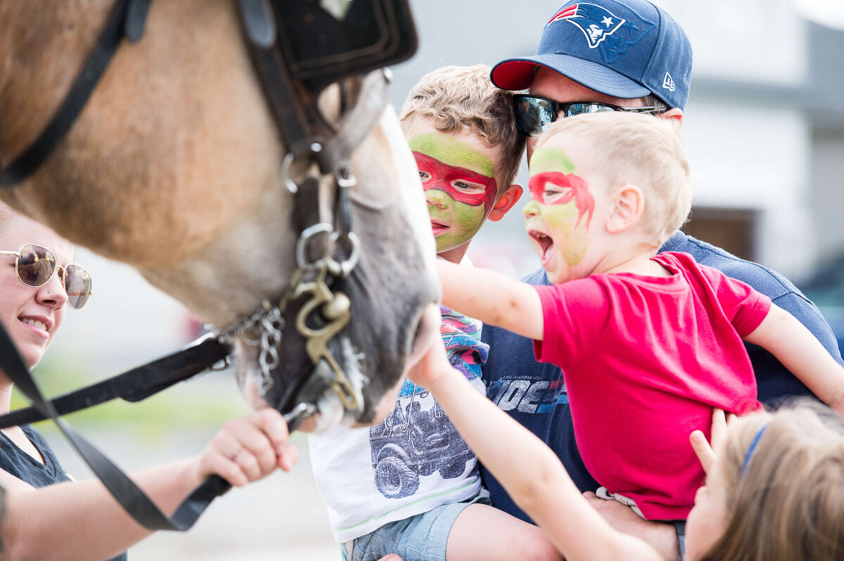 a little boy with face paint getting excited while he pats a horse during a corporate children's event.  Captured by Ottawa Event Photographer JEMMAN Photography COMMERCIAL