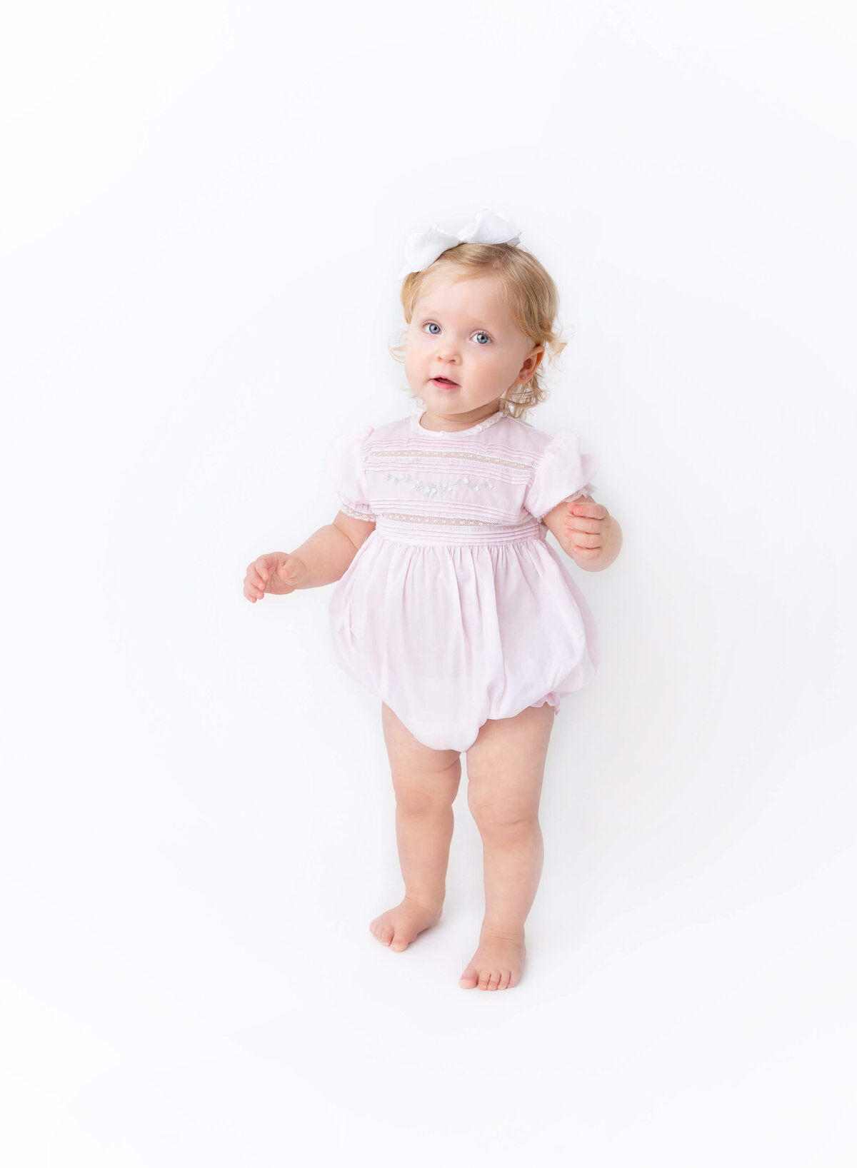 Standing portrait of a baby girl in a pastel pink dress and white bow — modern Heirloom baby photography session in Brooklyn, NYC.