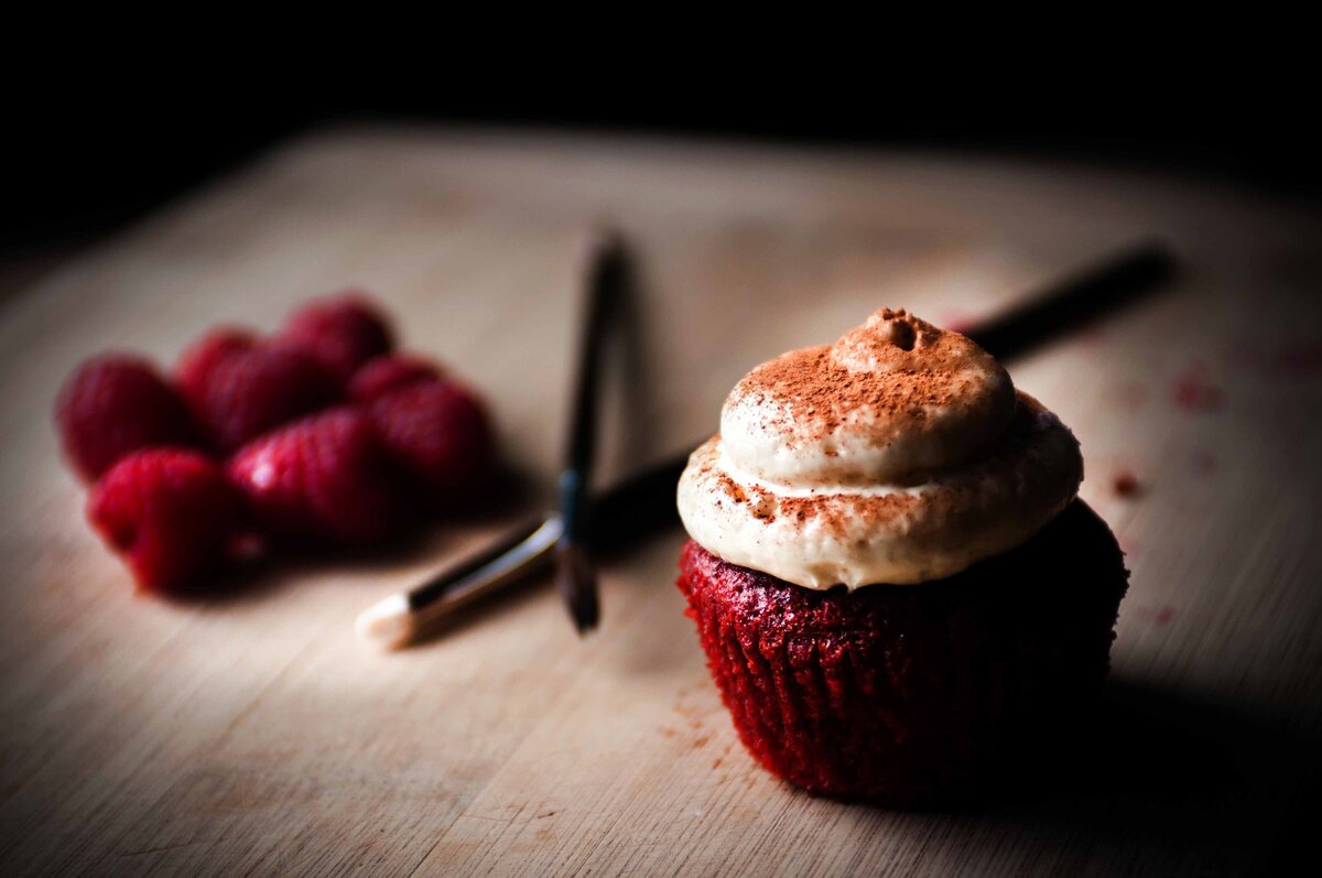 A red velvet cupcake with frosting dusted with cinnamon on a wood surface