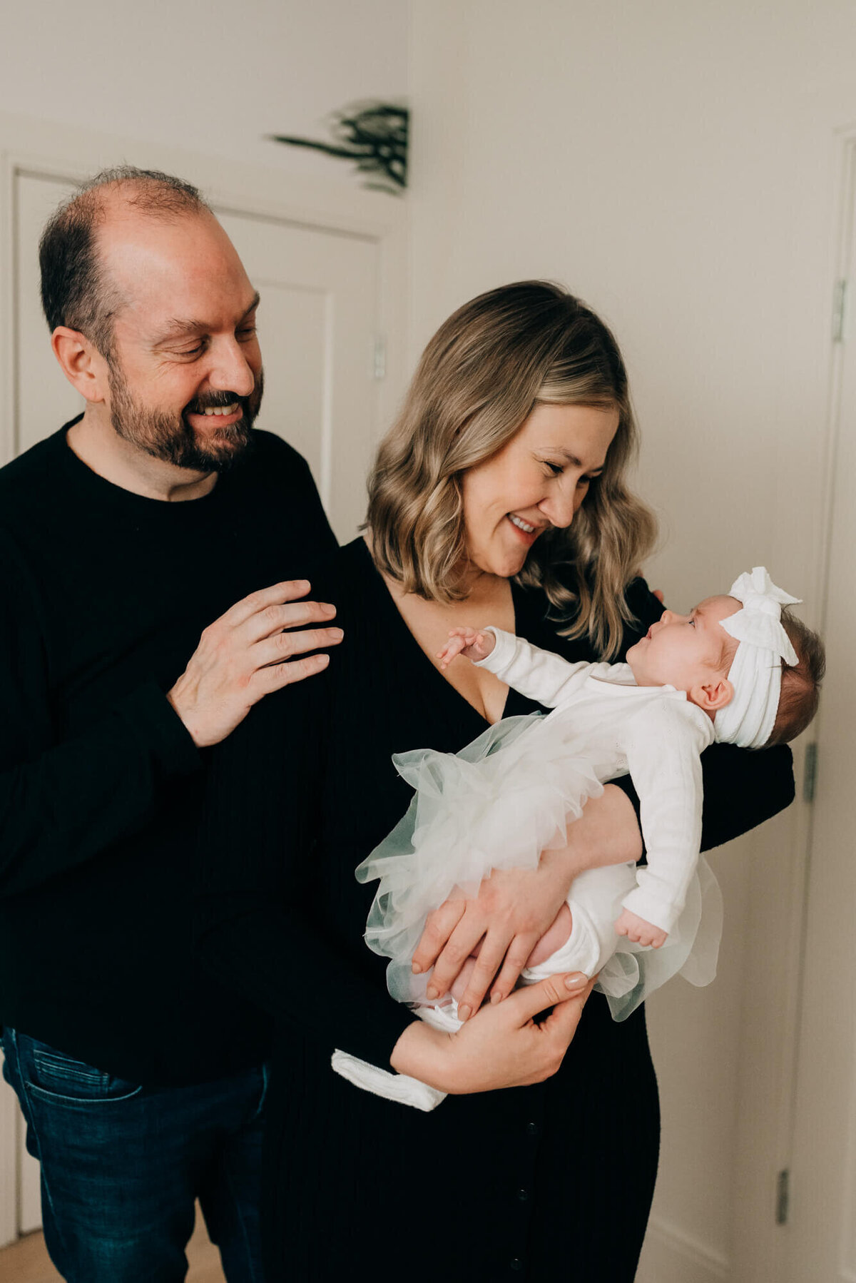 A baby in a cute white outfit is held by her mother and father in her safari themed nursery