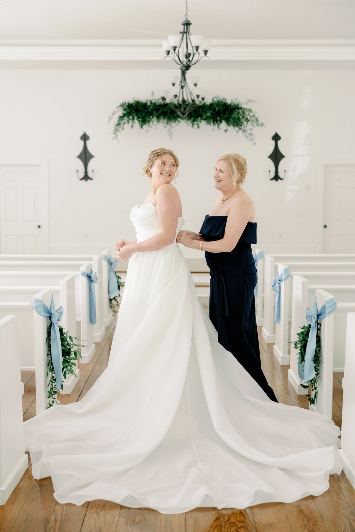 a woman helping a bride with her dress while they stand inside of a chapel