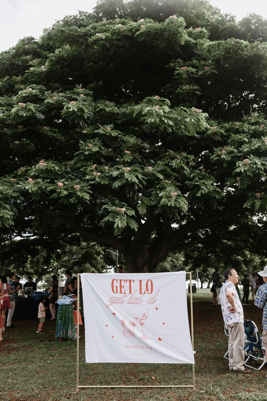Welcome dinner at Ala Moana Beach Park sign and guests mingling under large tree