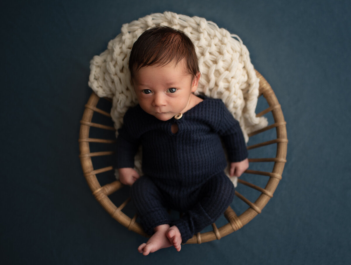 baby in a bowl and looking up with blue outfit at st. louis newborn photo shoot