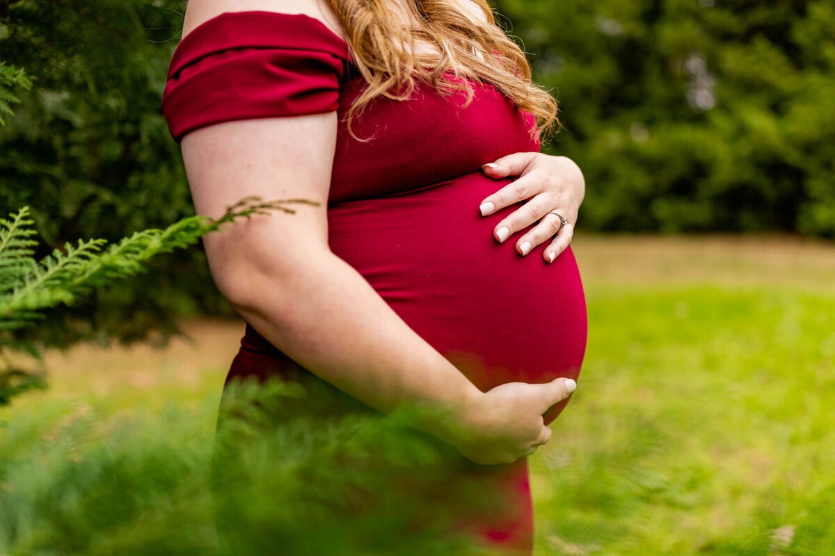 Pregnant mom in a maroon dress standing with some trees