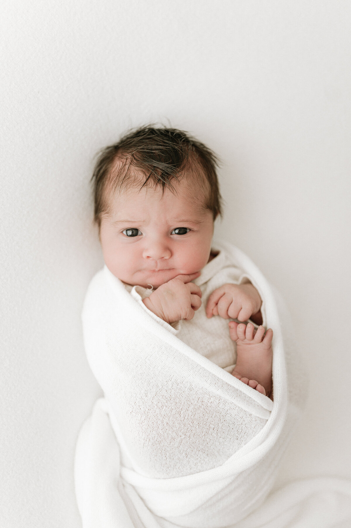 Newborn baby with lots of hair curled up in a blanket during a photoshoot