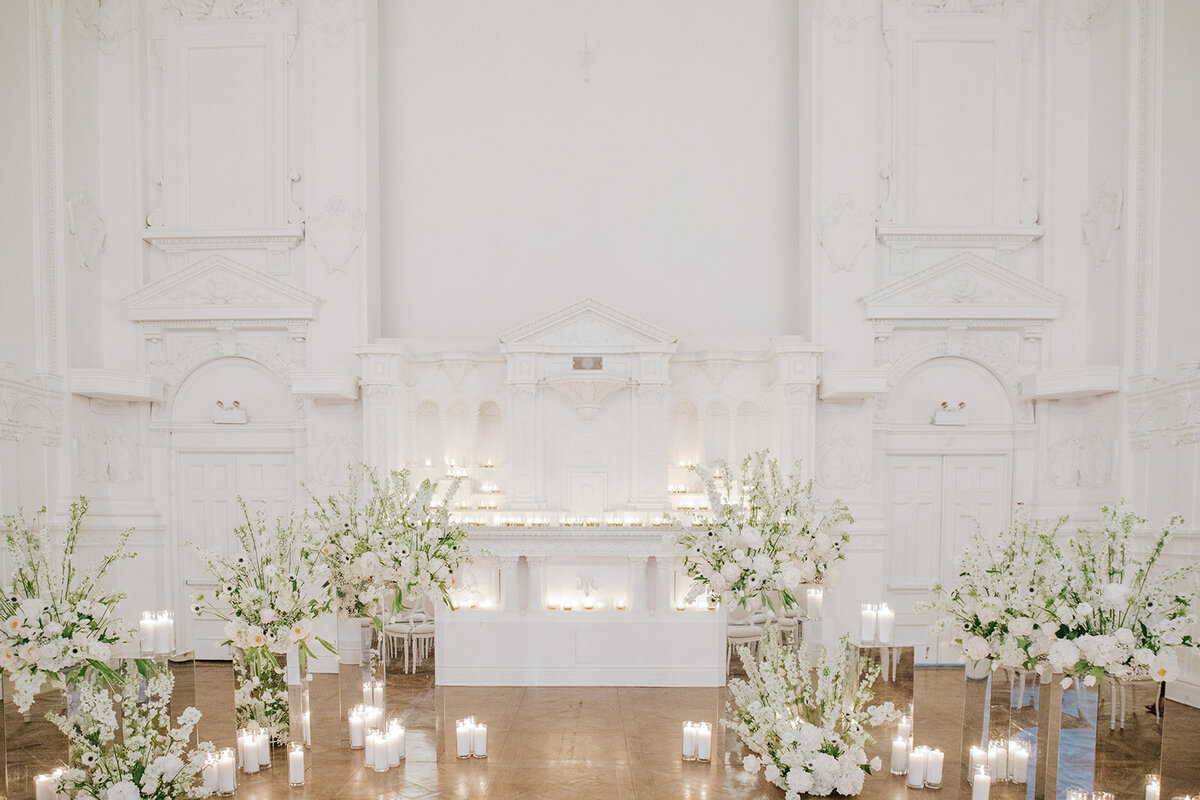  A wedding ceremony backdrop with candles and airy, elegant white arrangements at Maison Principale. 