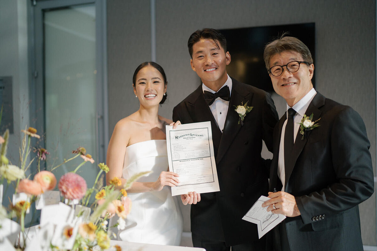 Bride and Groom pose with their wedding officiant and hold their Colorado Marriage license at the Aspen Meadows Resort wedding reception venue.