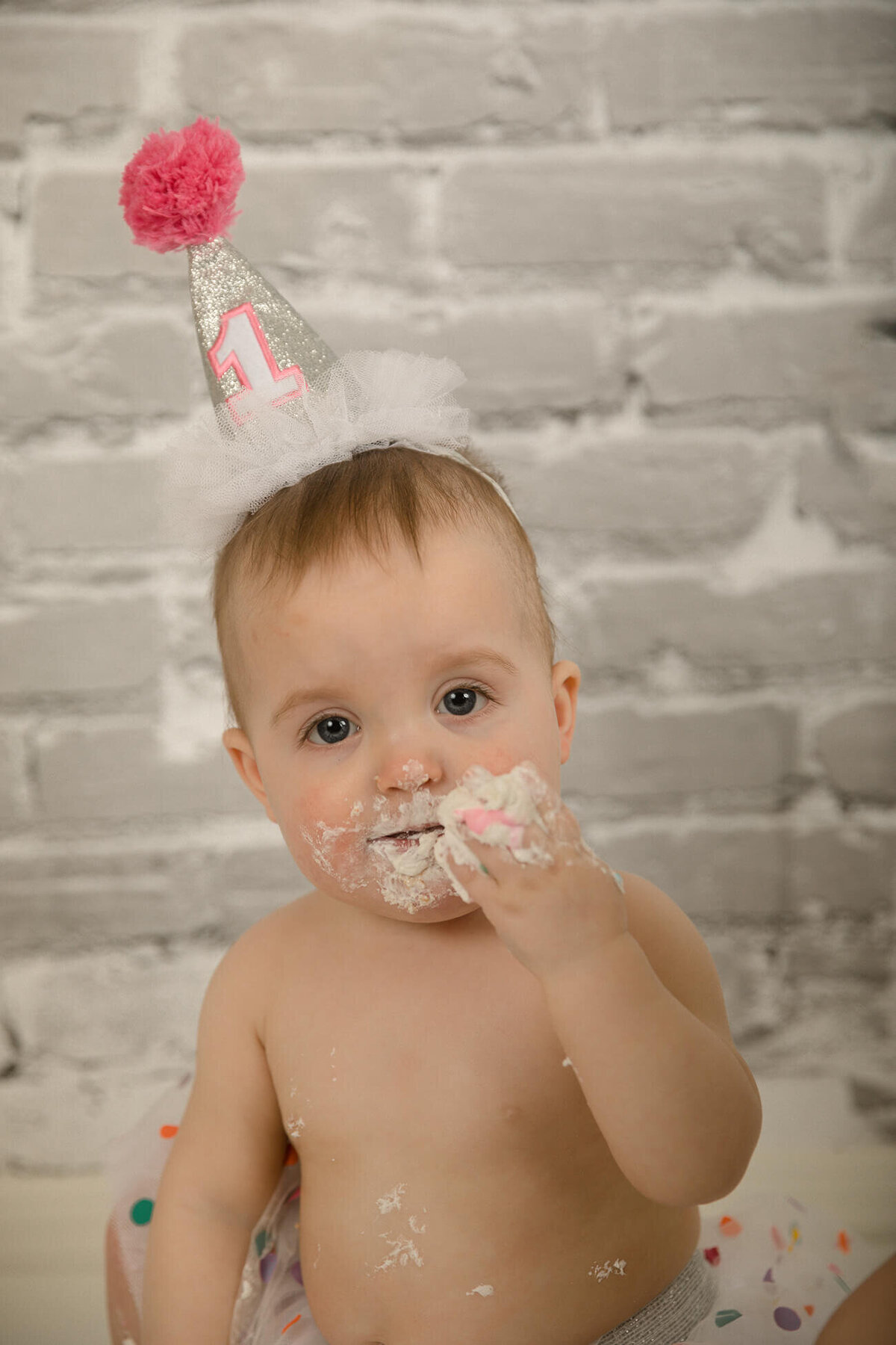 1 year old girl with party hat eating cake.