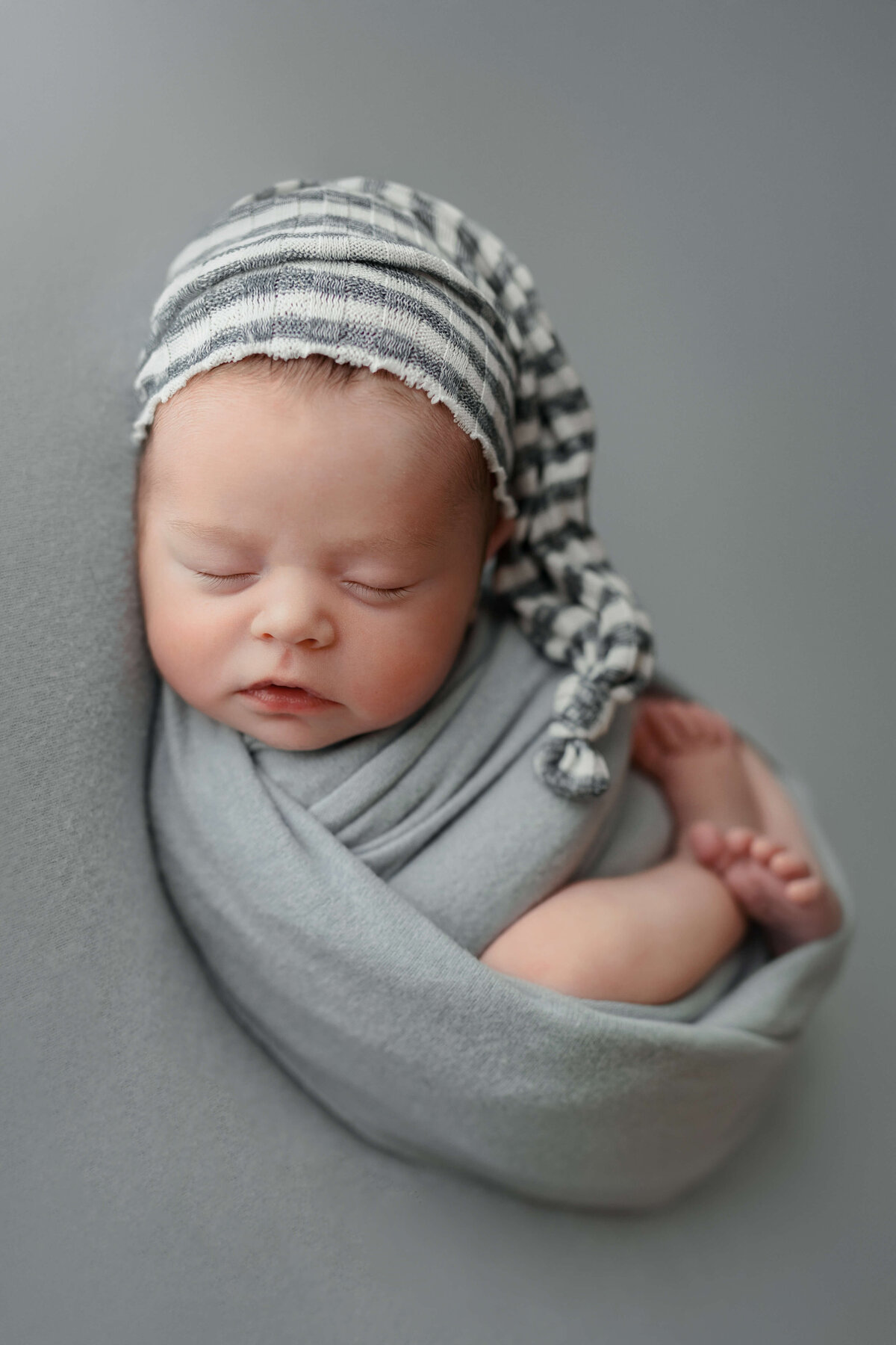 baby boy wearing striped  sleepy cap on blue backdrop in newborn  session