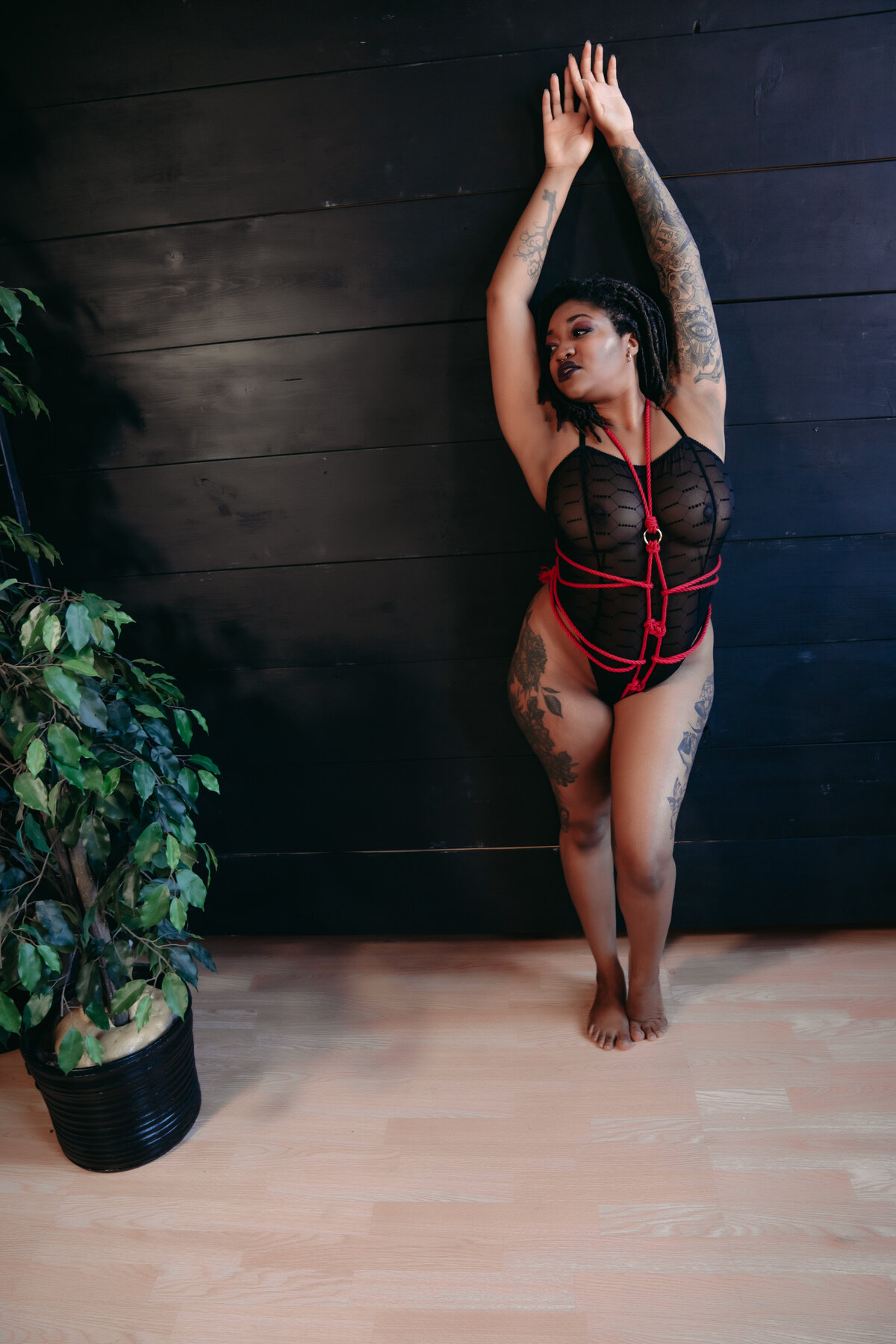 A stunning black woman  wearing black lingerie and shibari inspired red rope ties around her