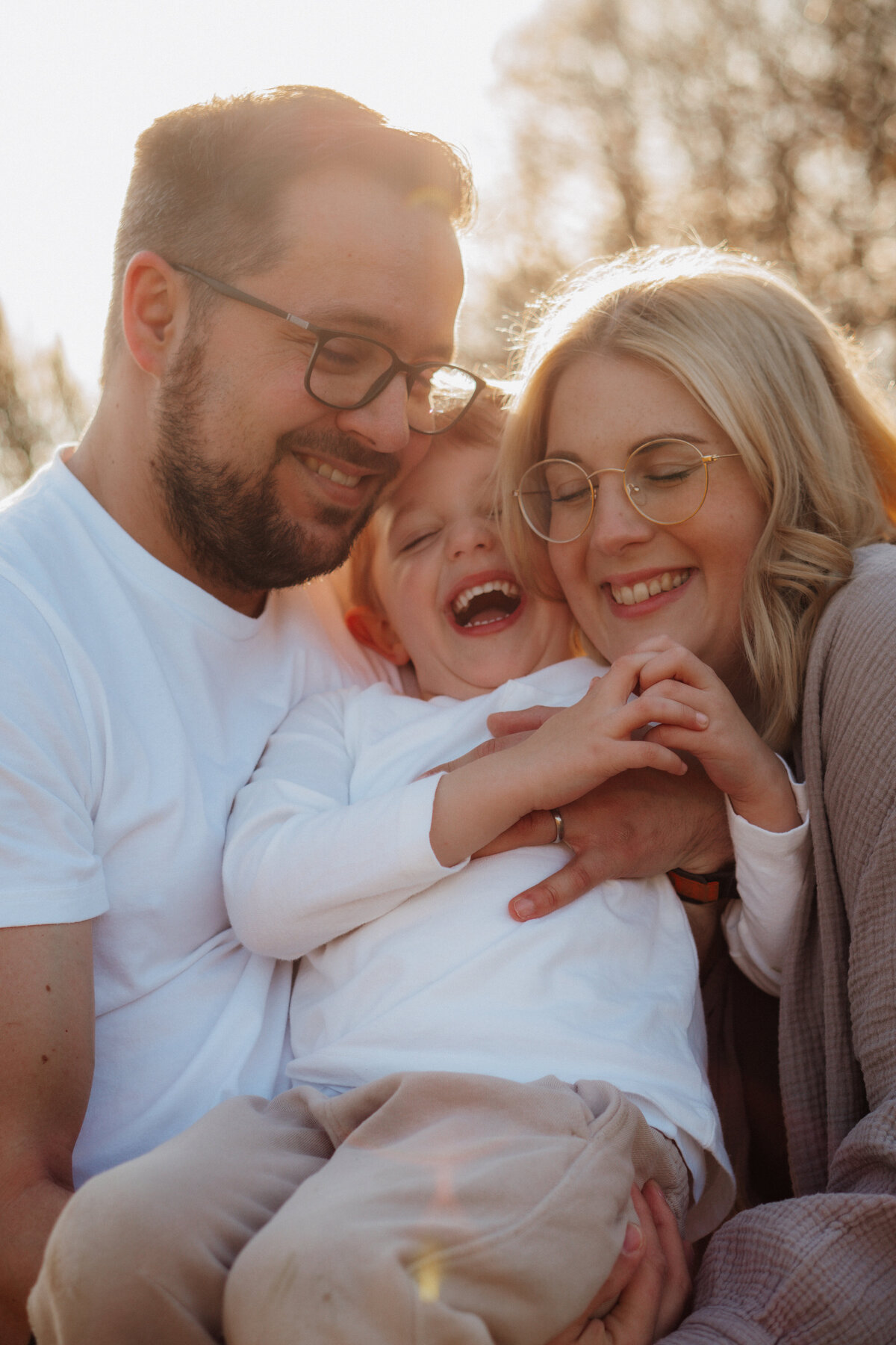 Papa, Mama und Kind kuscheln miteinander im Sonnenuntergang und lachen gemeinsam