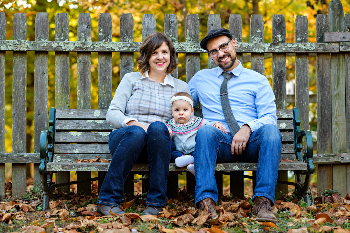 A family portrait of new parents and a baby on a bench in a philadelphia park.